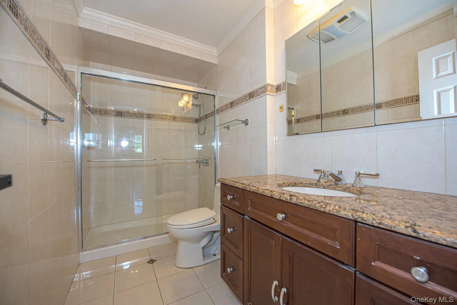 Full bathroom with tile walls, vanity, crown molding, a stall shower, and light tile patterned flooring Full bathroom with tile walls, vanity, crown molding, a stall shower, and light tile patterned flooring