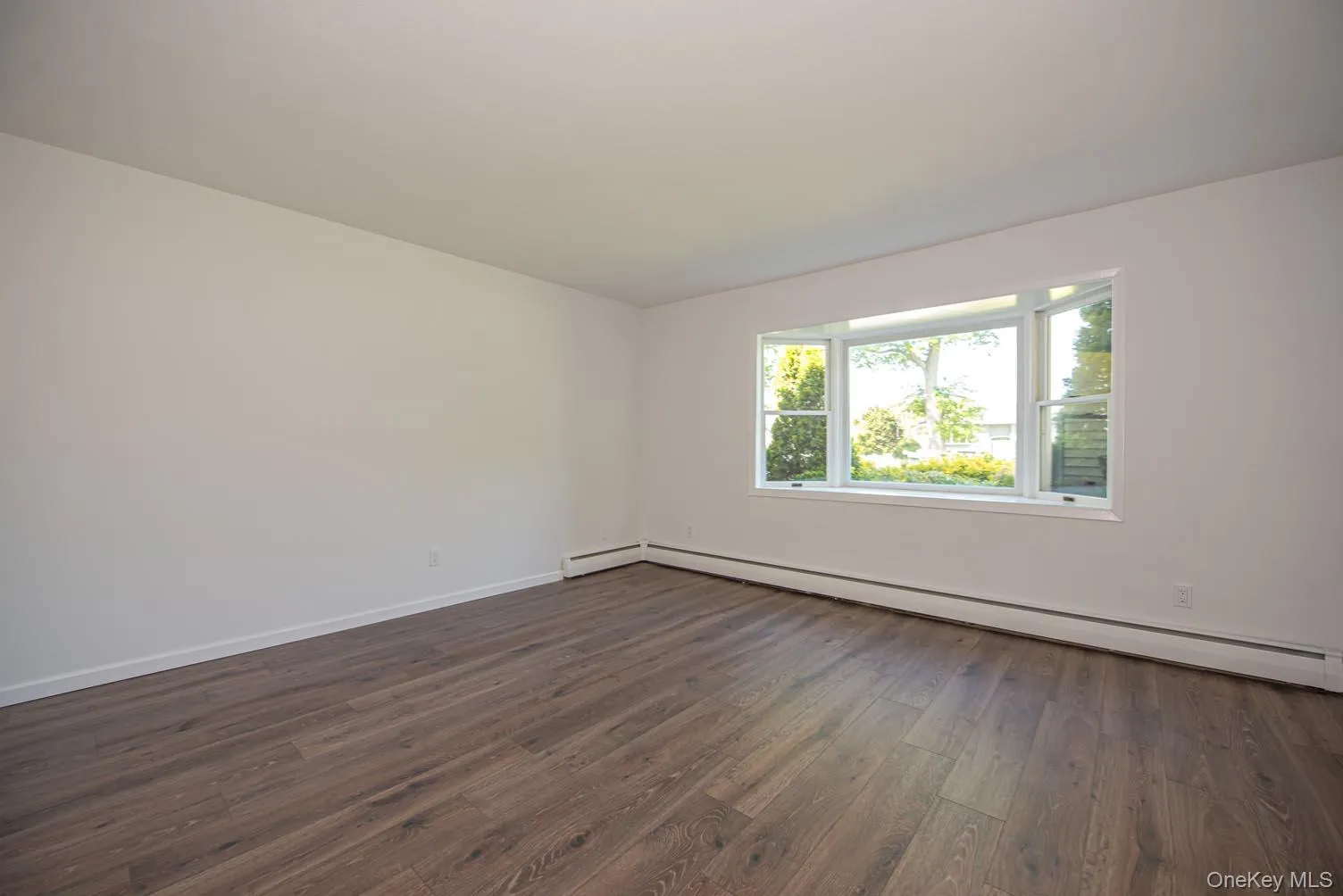Unfurnished room with dark wood finished floors and baseboard heating Unfurnished room with dark wood finished floors and baseboard heating