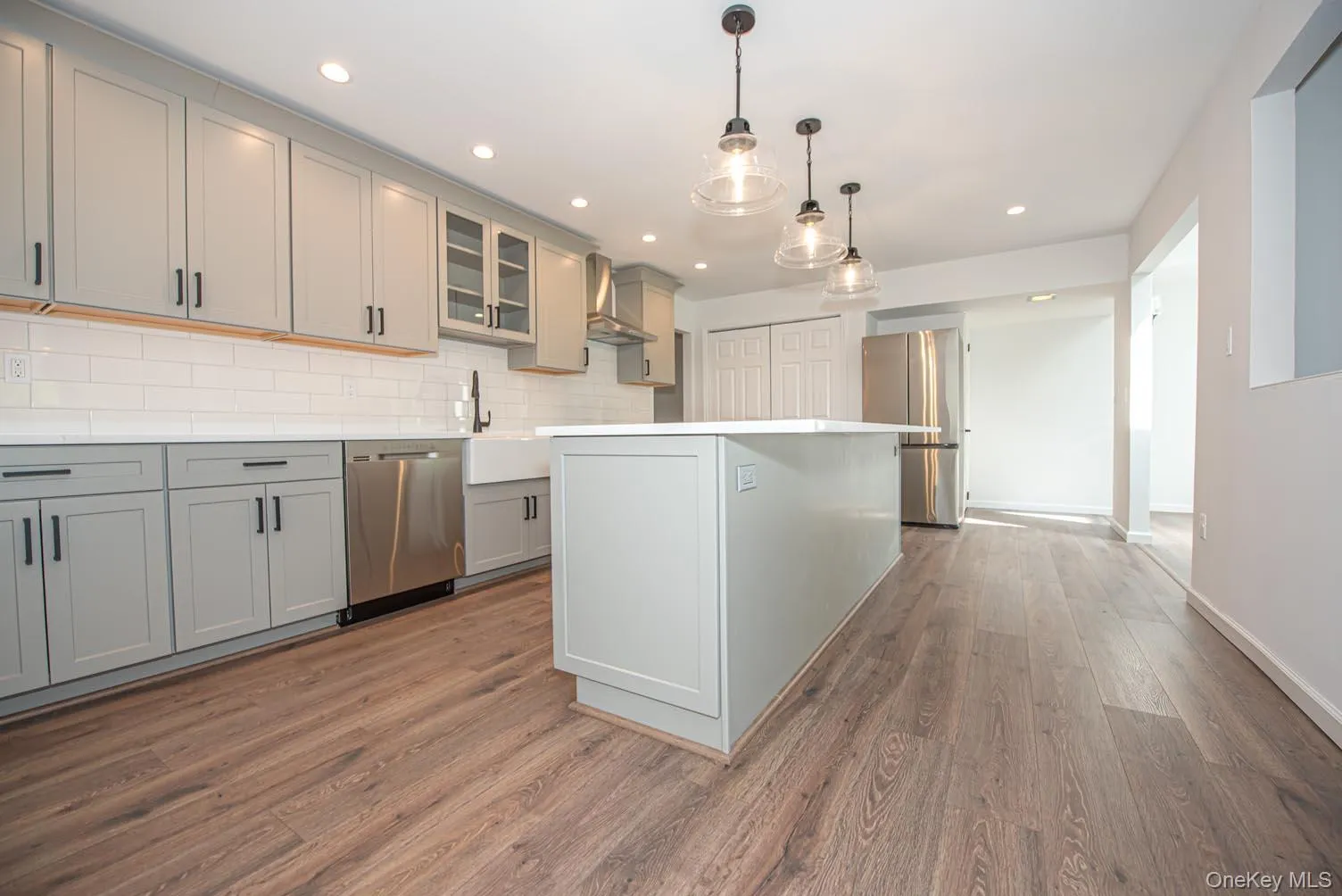 Kitchen with gray cabinets, glass insert cabinets, appliances with stainless steel finishes, hanging light fixtures, and dark wood-type flooring Kitchen with gray cabinets, glass insert cabinets, appliances with stainless steel finishes, hanging light fixtures, and dark wood-type flooring