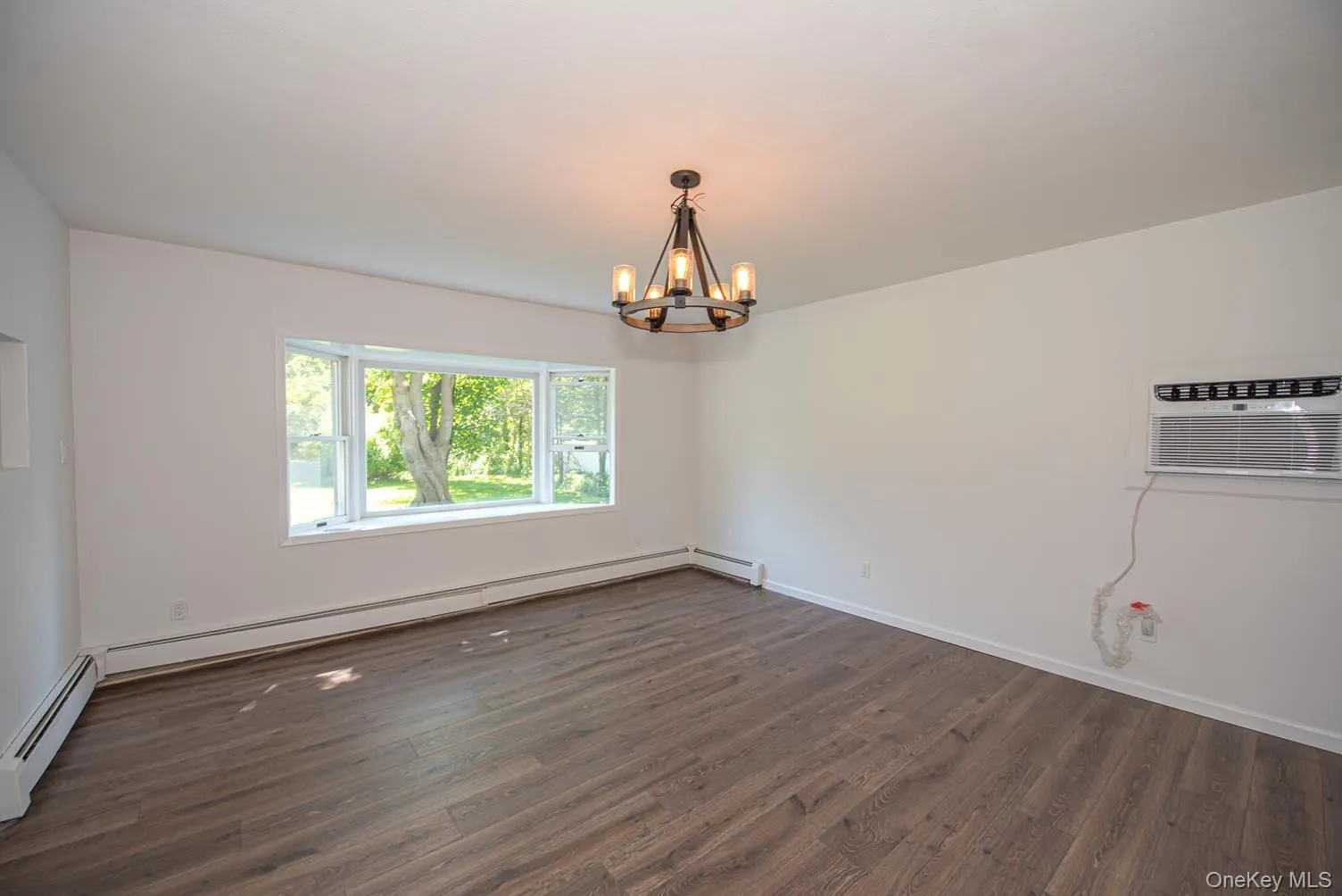 Unfurnished room with dark wood-style floors, a chandelier, a wall mounted AC, and a baseboard heating unit Unfurnished room with dark wood-style floors, a chandelier, a wall mounted AC, and a baseboard heating unit