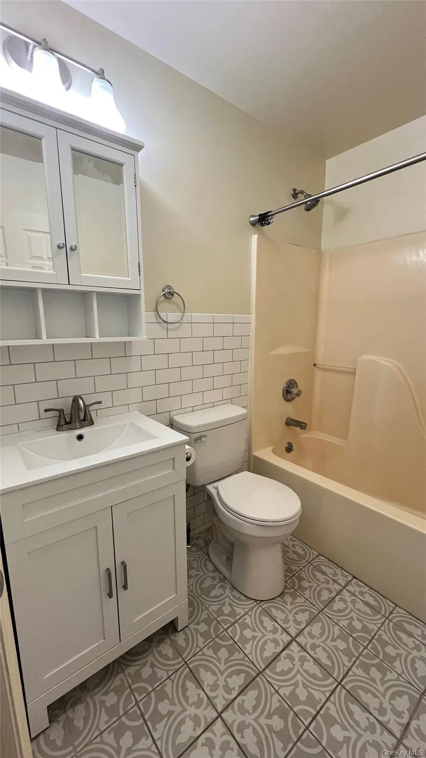 Full bath featuring tile walls, vanity, wainscoting, bathtub / shower combination, and light tile patterned flooring Full bath featuring tile walls, vanity, wainscoting, bathtub / shower combination, and light tile patterned flooring