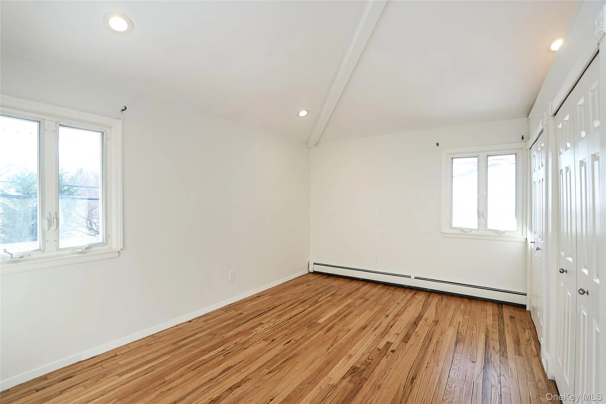 Unfurnished room with light wood finished floors, baseboard heating, recessed lighting, plenty of natural light, and lofted ceiling Unfurnished room with light wood finished floors, baseboard heating, recessed lighting, plenty of natural light, and lofted ceiling