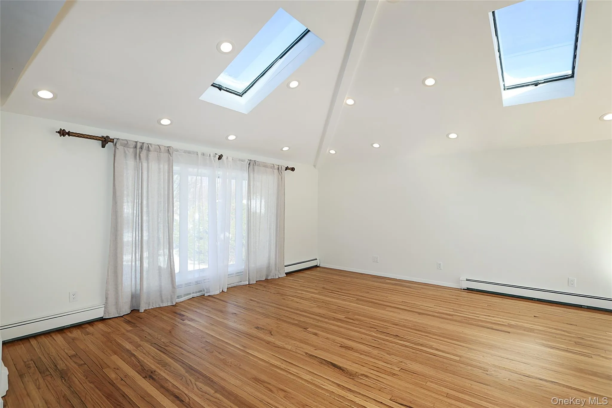 Unfurnished room with vaulted ceiling, recessed lighting, a skylight, light wood finished floors, and a baseboard radiator Unfurnished room with vaulted ceiling, recessed lighting, a skylight, light wood finished floors, and a baseboard radiator