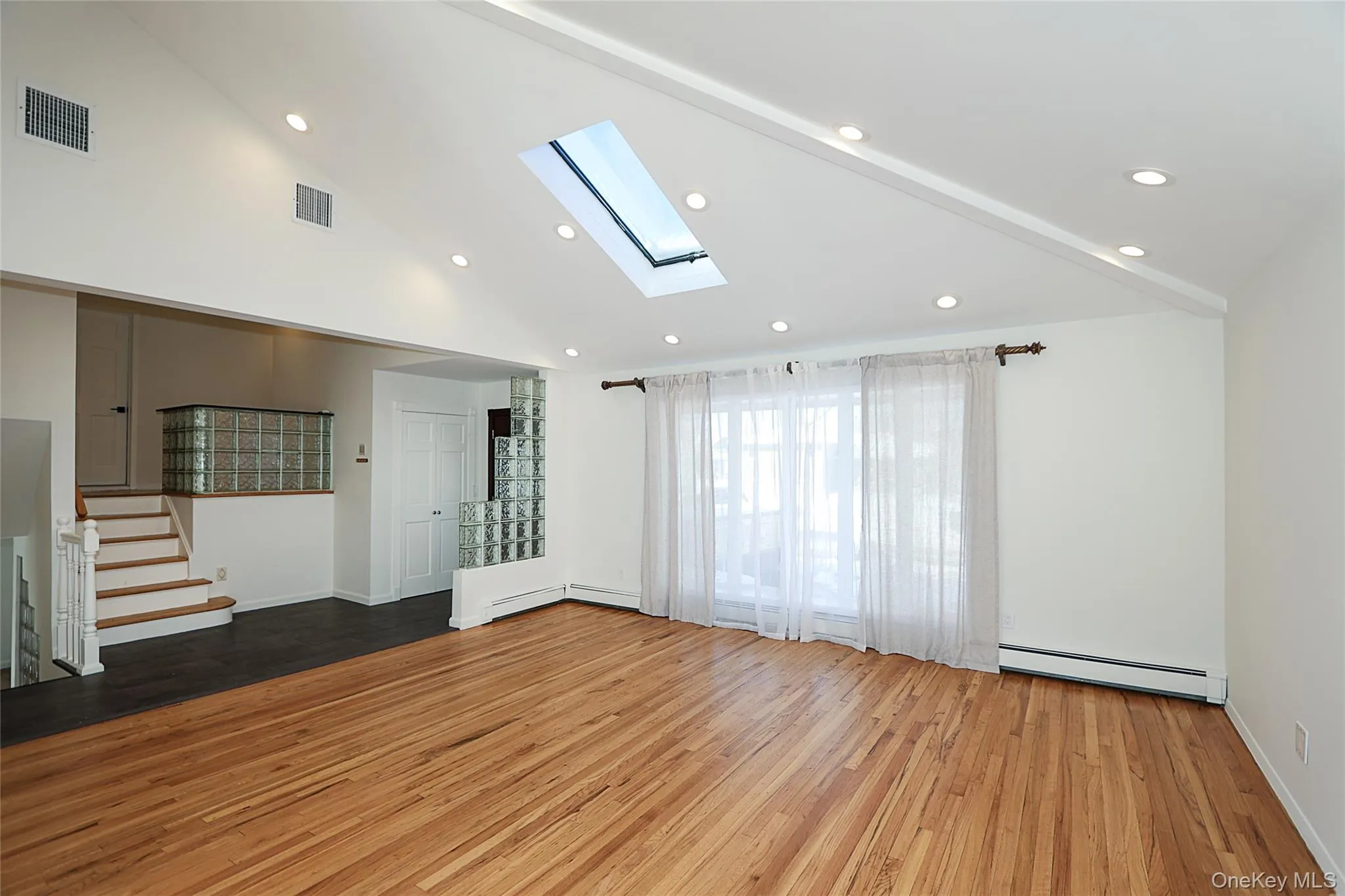 Unfurnished living room with a skylight, hardwood / wood-style flooring, recessed lighting, high vaulted ceiling, and baseboard heating Unfurnished living room with a skylight, hardwood / wood-style flooring, recessed lighting, high vaulted ceiling, and baseboard heating