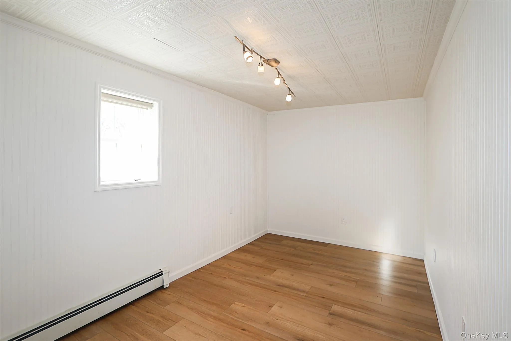 Unfurnished room with a baseboard heating unit, an ornate ceiling, light wood-style floors, track lighting, and ornamental molding Unfurnished room with a baseboard heating unit, an ornate ceiling, light wood-style floors, track lighting, and ornamental molding