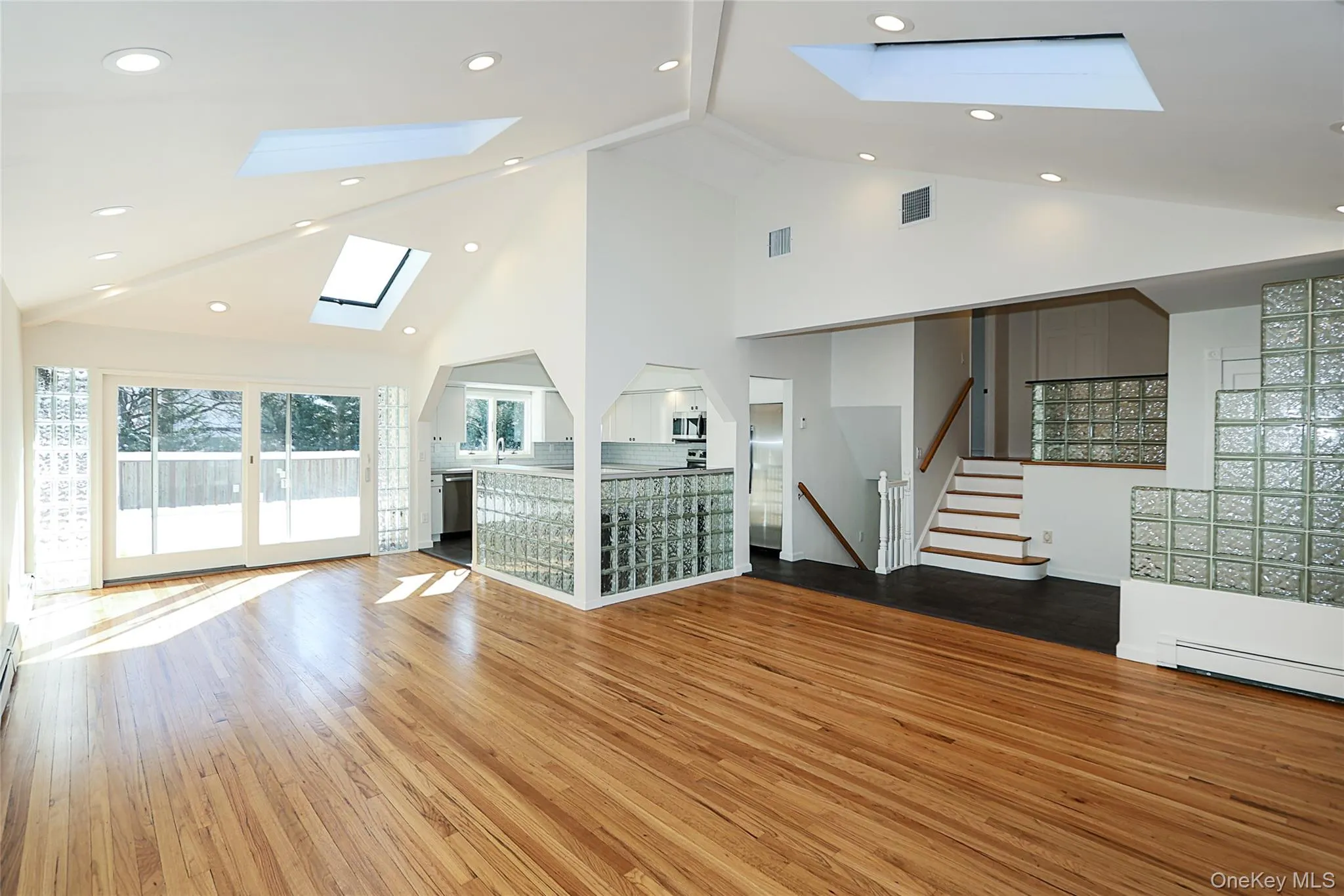 Unfurnished living room with high vaulted ceiling, hardwood / wood-style flooring, a skylight, stairway, and recessed lighting Unfurnished living room with high vaulted ceiling, hardwood / wood-style flooring, a skylight, stairway, and recessed lighting