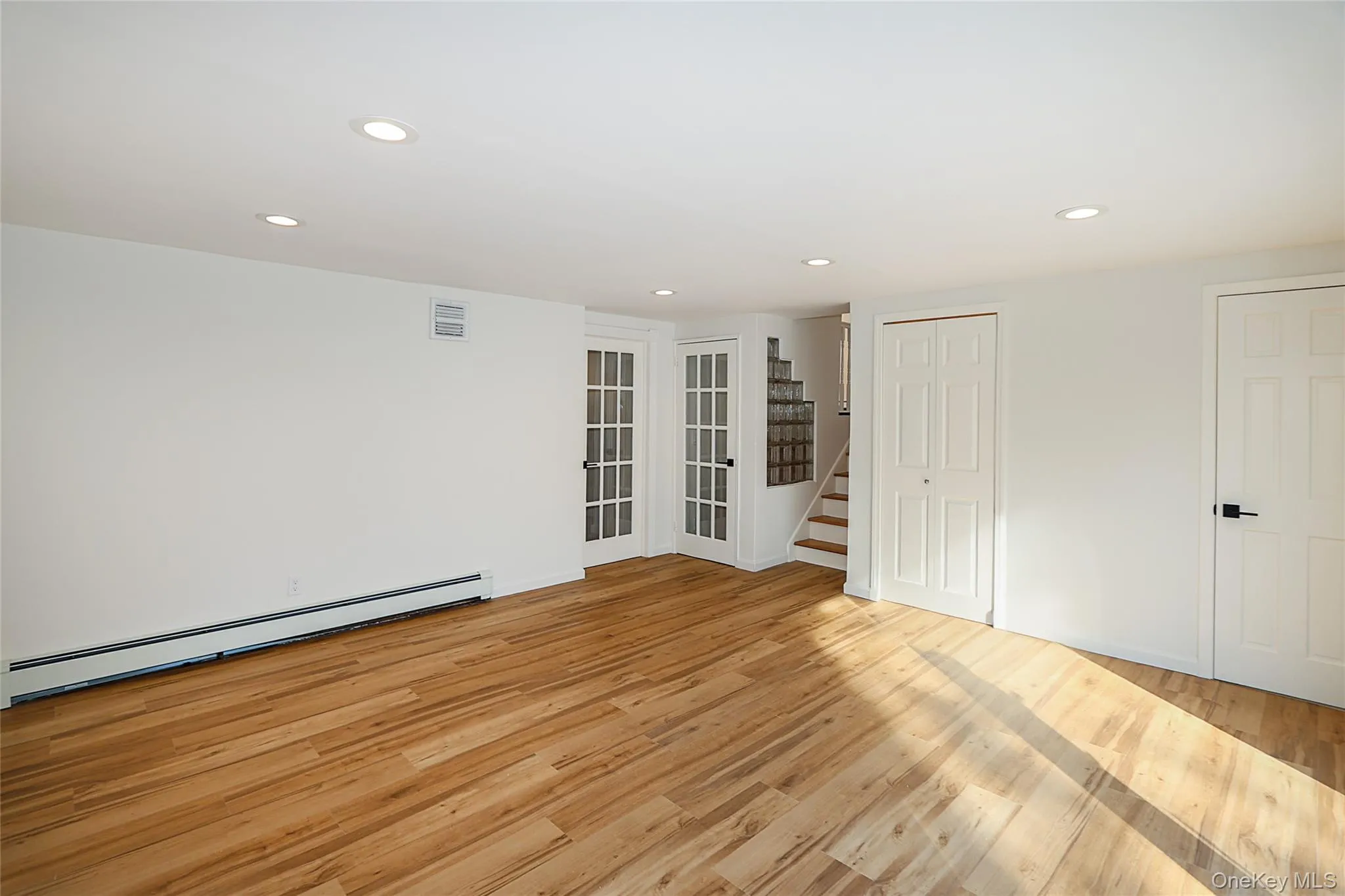 Spare room featuring recessed lighting, baseboard heating, stairway, and light wood-style floors Spare room featuring recessed lighting, baseboard heating, stairway, and light wood-style floors