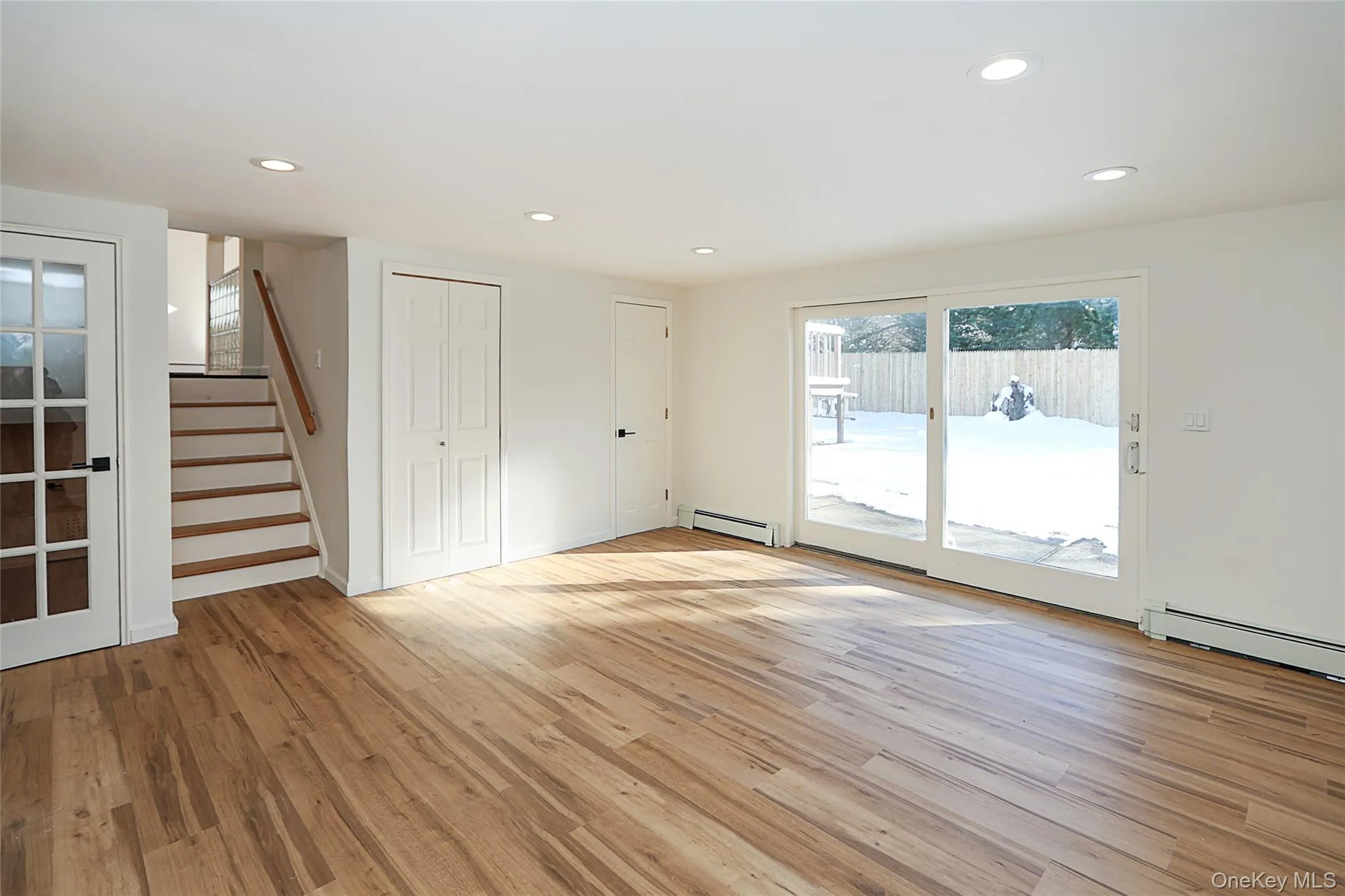 Unfurnished living room with stairway, light wood-type flooring, recessed lighting, and a baseboard radiator Unfurnished living room with stairway, light wood-type flooring, recessed lighting, and a baseboard radiator