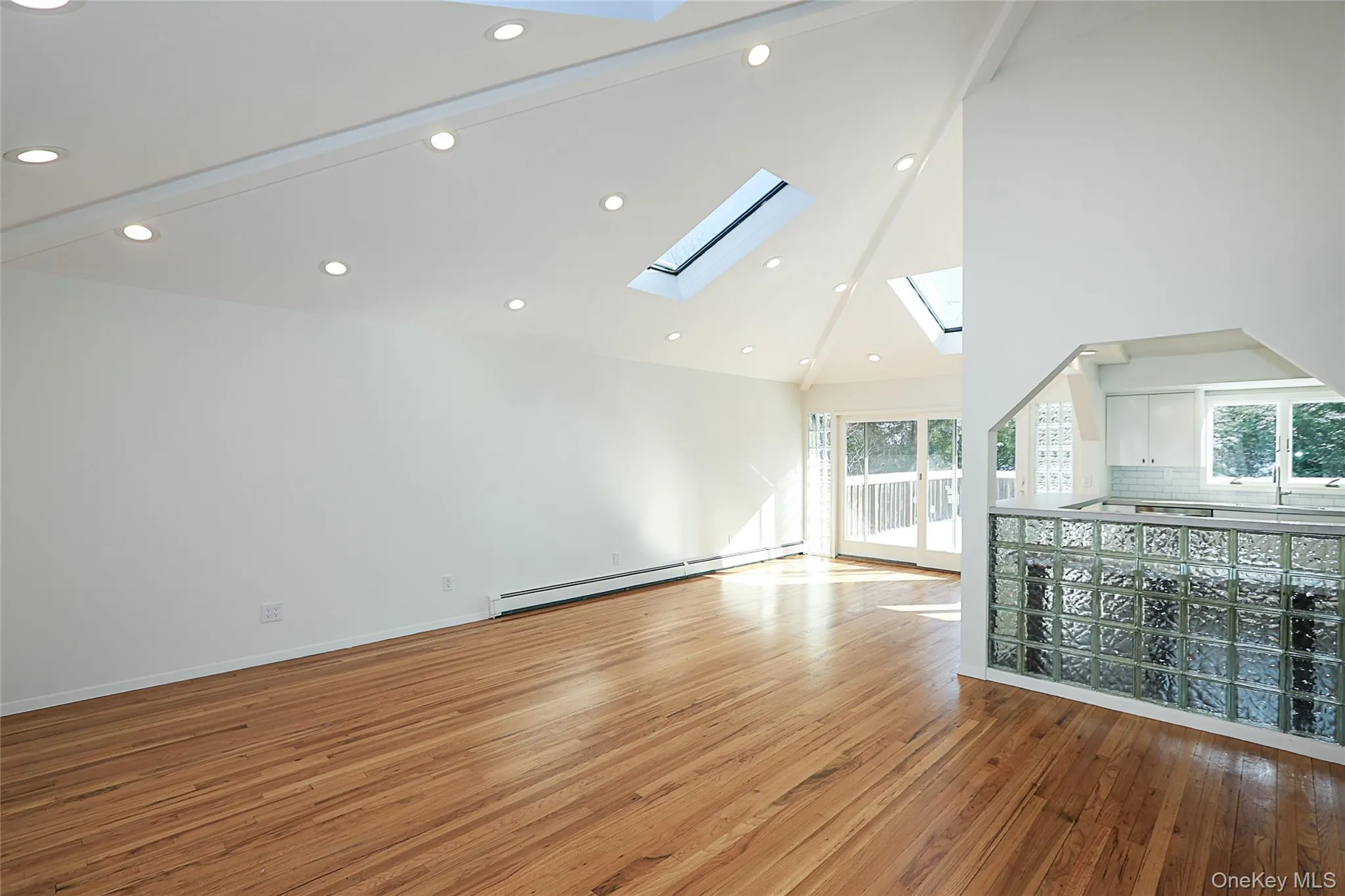 Unfurnished living room featuring high vaulted ceiling, baseboard heating, light wood finished floors, a skylight, and recessed lighting Unfurnished living room featuring high vaulted ceiling, baseboard heating, light wood finished floors, a skylight, and recessed lighting