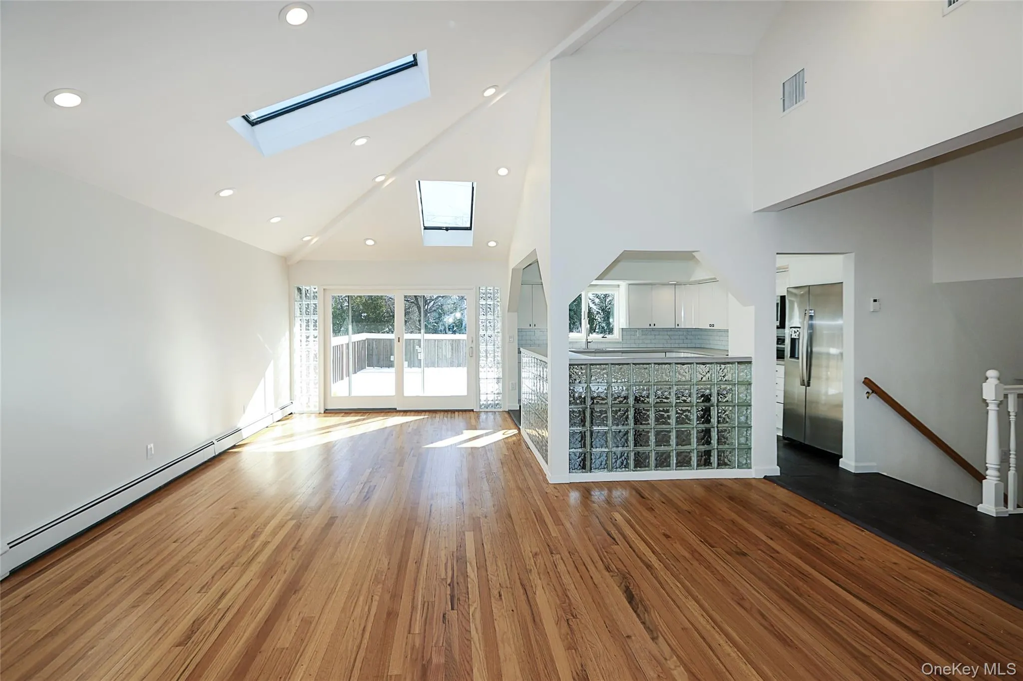 Unfurnished living room with high vaulted ceiling, dark wood finished floors, a baseboard heating unit, and a skylight Unfurnished living room with high vaulted ceiling, dark wood finished floors, a baseboard heating unit, and a skylight