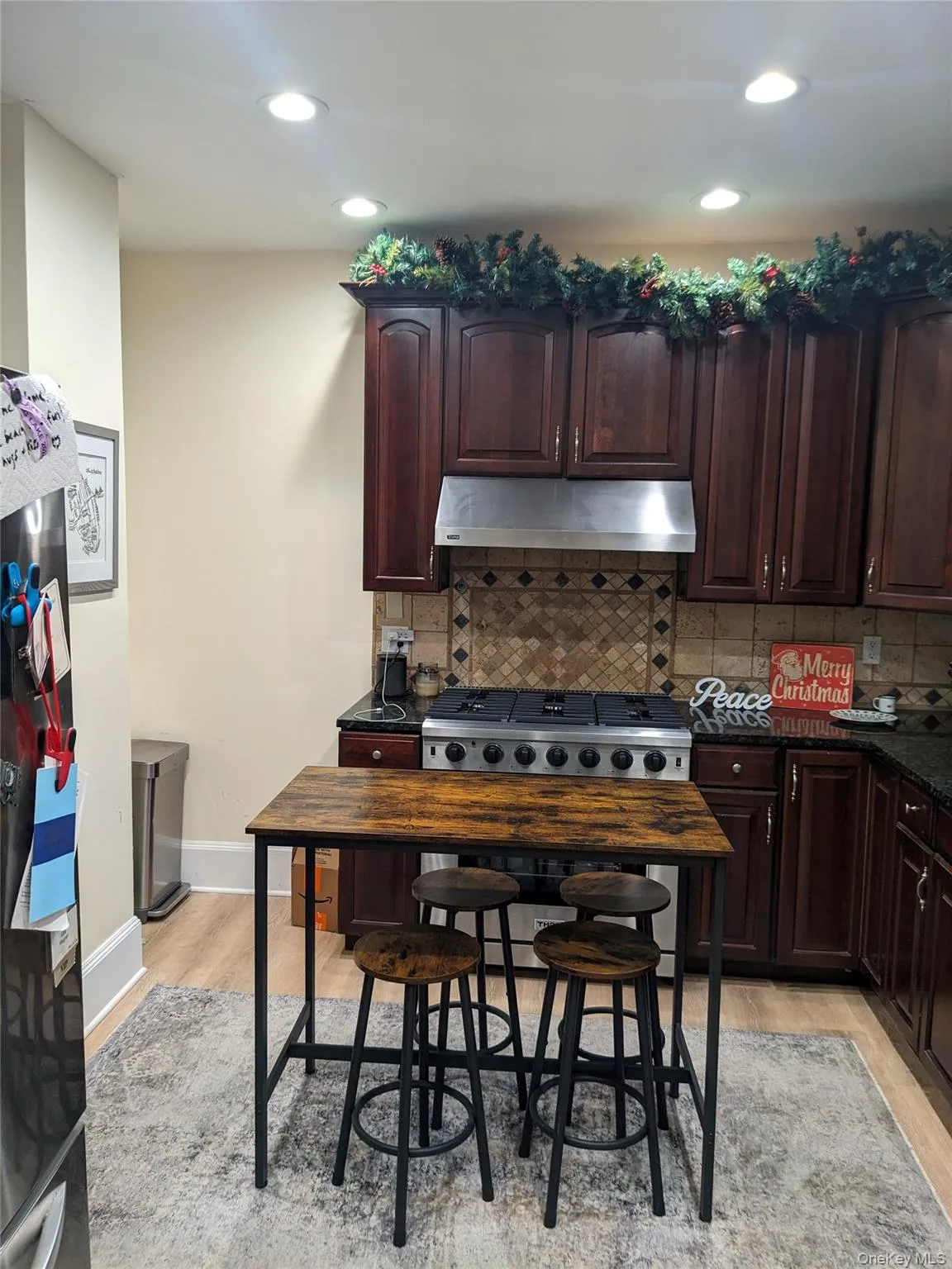 Kitchen with dark brown cabinets, under cabinet range hood, recessed lighting, dark stone counters, and light wood-style floors Kitchen with dark brown cabinets, under cabinet range hood, recessed lighting, dark stone counters, and light wood-style floors