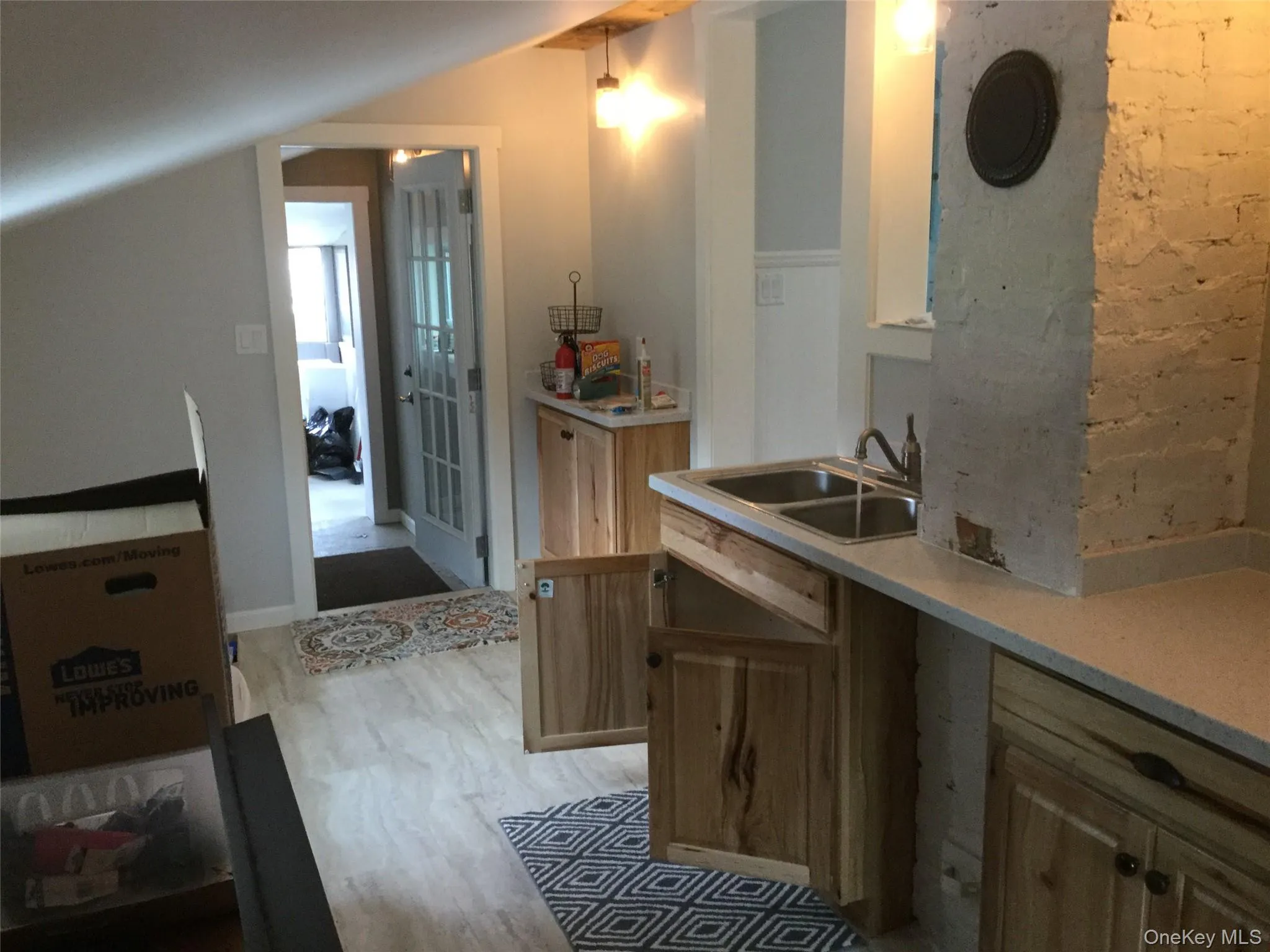 Kitchen featuring light wood finished floors, brick wall, lofted ceiling, and light stone countertops Kitchen featuring light wood finished floors, brick wall, lofted ceiling, and light stone countertops