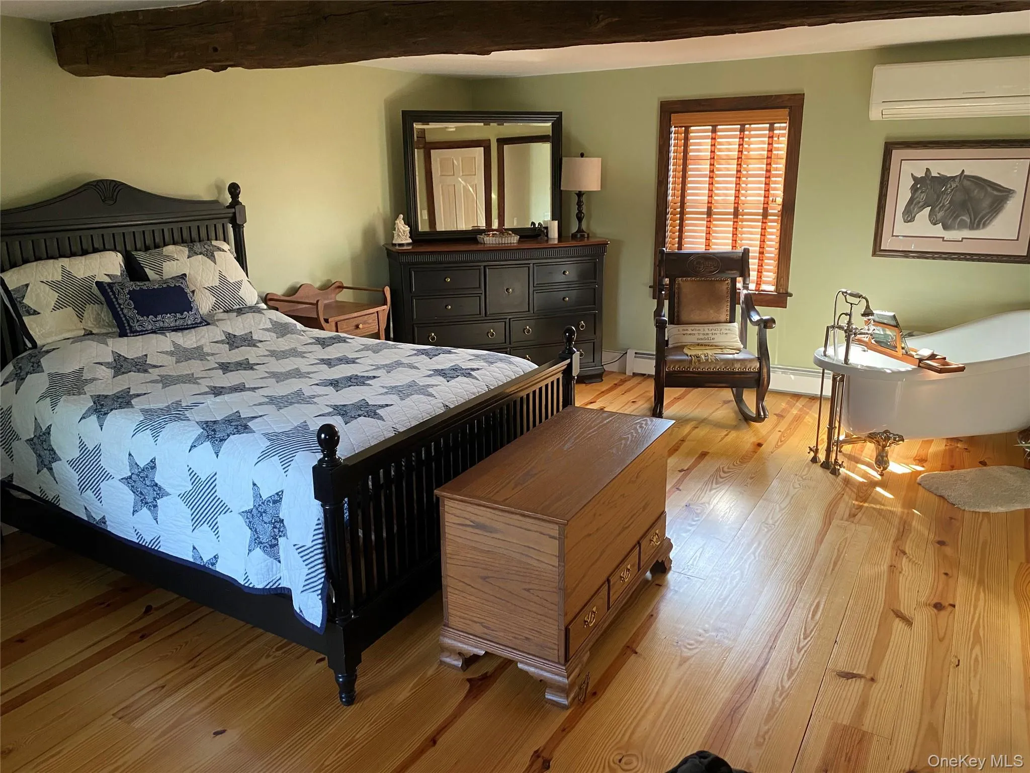 Bedroom with an AC wall unit, light wood-type flooring, and a baseboard radiator Bedroom with an AC wall unit, light wood-type flooring, and a baseboard radiator