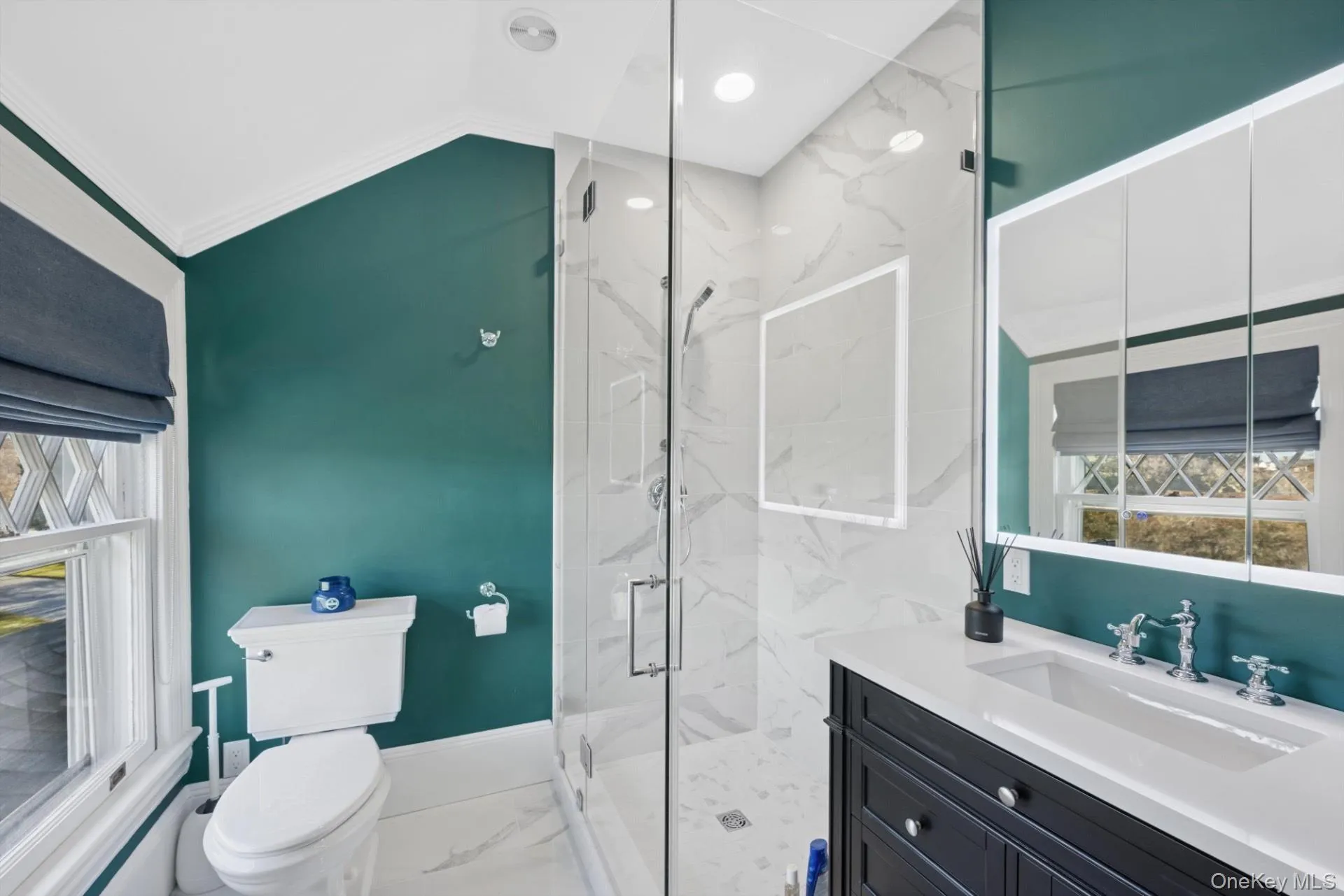 Bathroom featuring light marble finish floors, vanity, a marble finish shower, vaulted ceiling, and crown molding Bathroom featuring light marble finish floors, vanity, a marble finish shower, vaulted ceiling, and crown molding