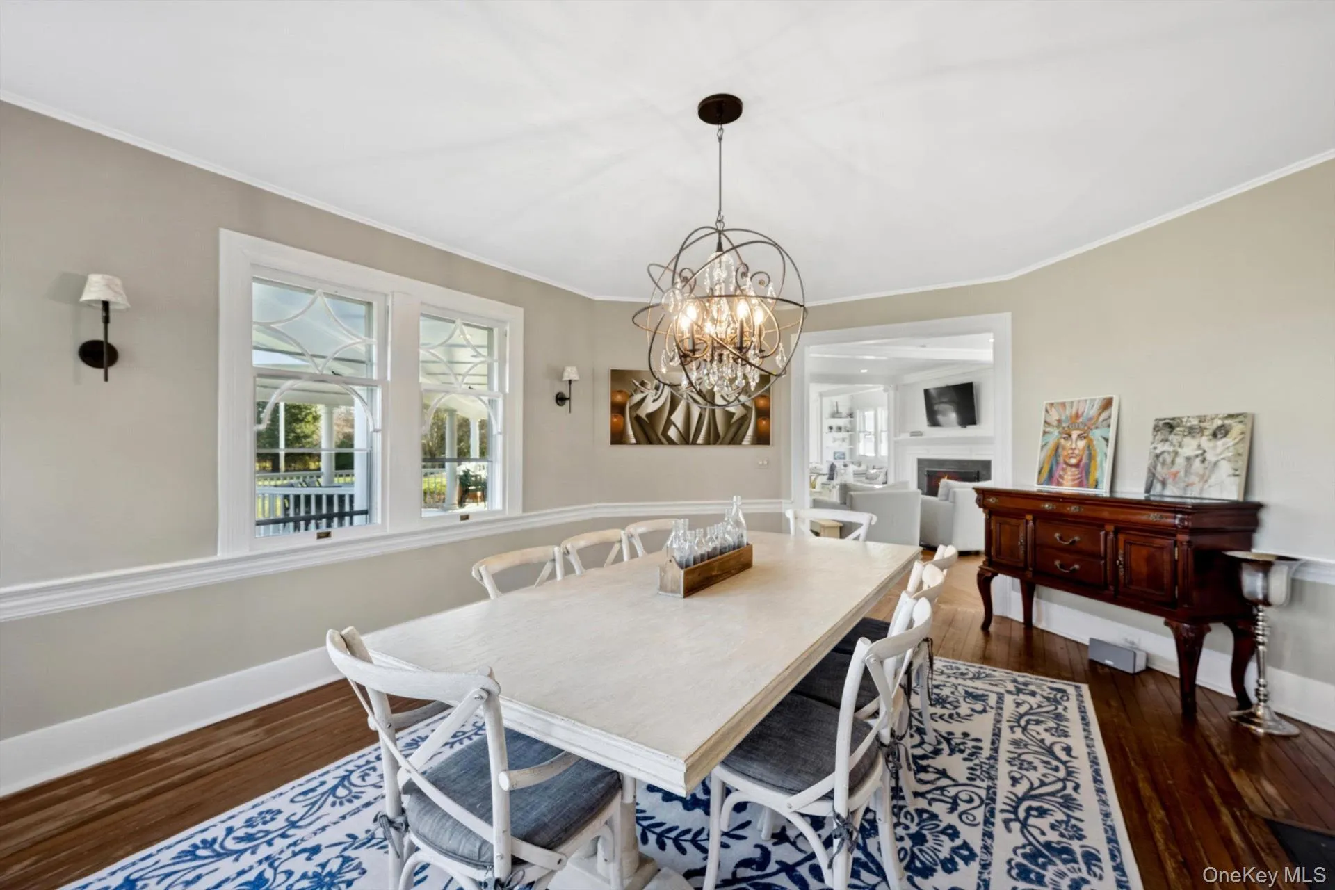 Dining space featuring dark wood-style floors, ornamental molding, a chandelier, and a warm lit fireplace Dining space featuring dark wood-style floors, ornamental molding, a chandelier, and a warm lit fireplace