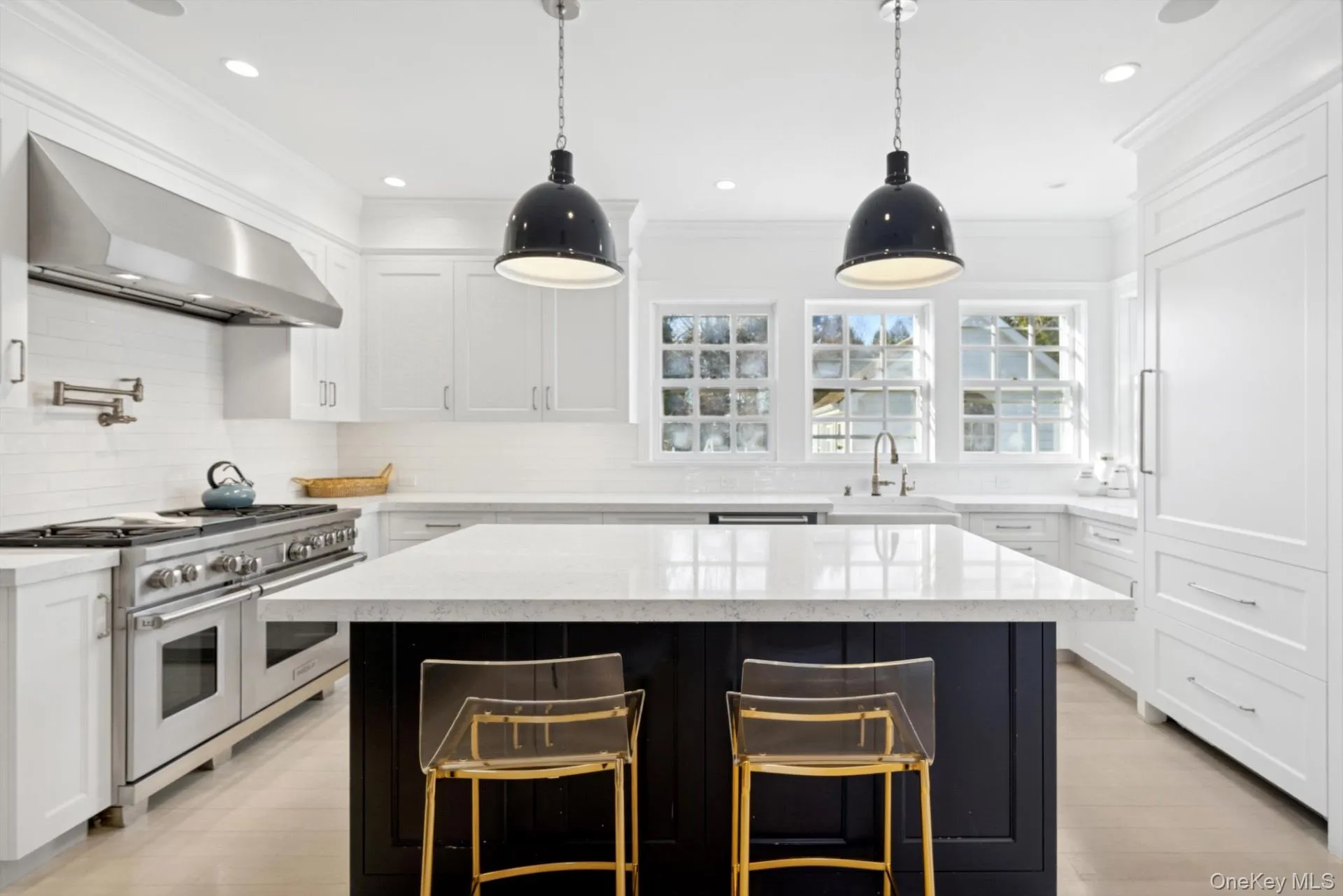 Kitchen featuring dark cabinetry, light stone counters, double oven range, decorative light fixtures, and ornamental molding Kitchen featuring dark cabinetry, light stone counters, double oven range, decorative light fixtures, and ornamental molding