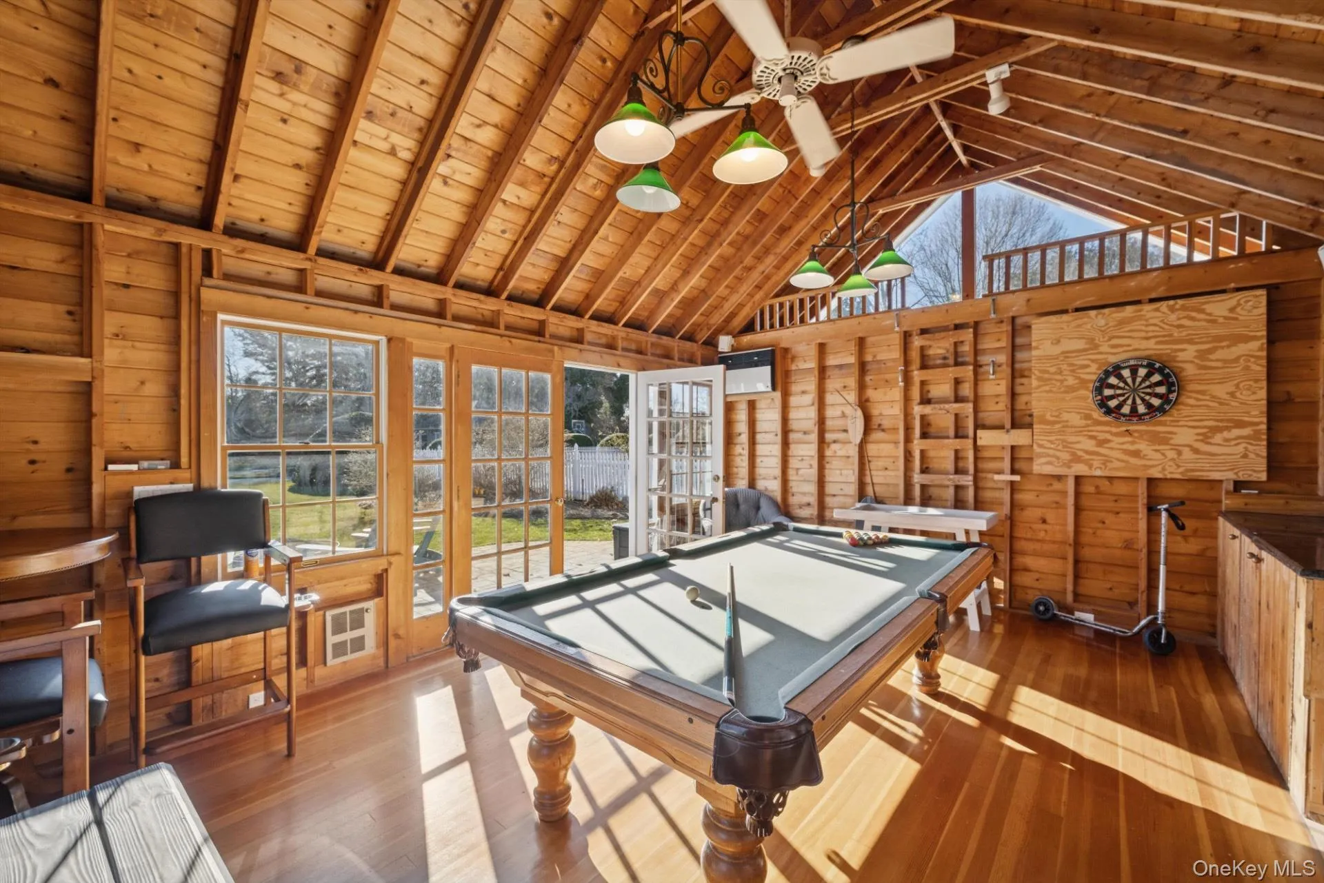 Recreation room with high vaulted ceiling, wood walls, wood-type flooring, a ceiling fan, and a wooden ceiling with exposed beams Recreation room with high vaulted ceiling, wood walls, wood-type flooring, a ceiling fan, and a wooden ceiling with exposed beams