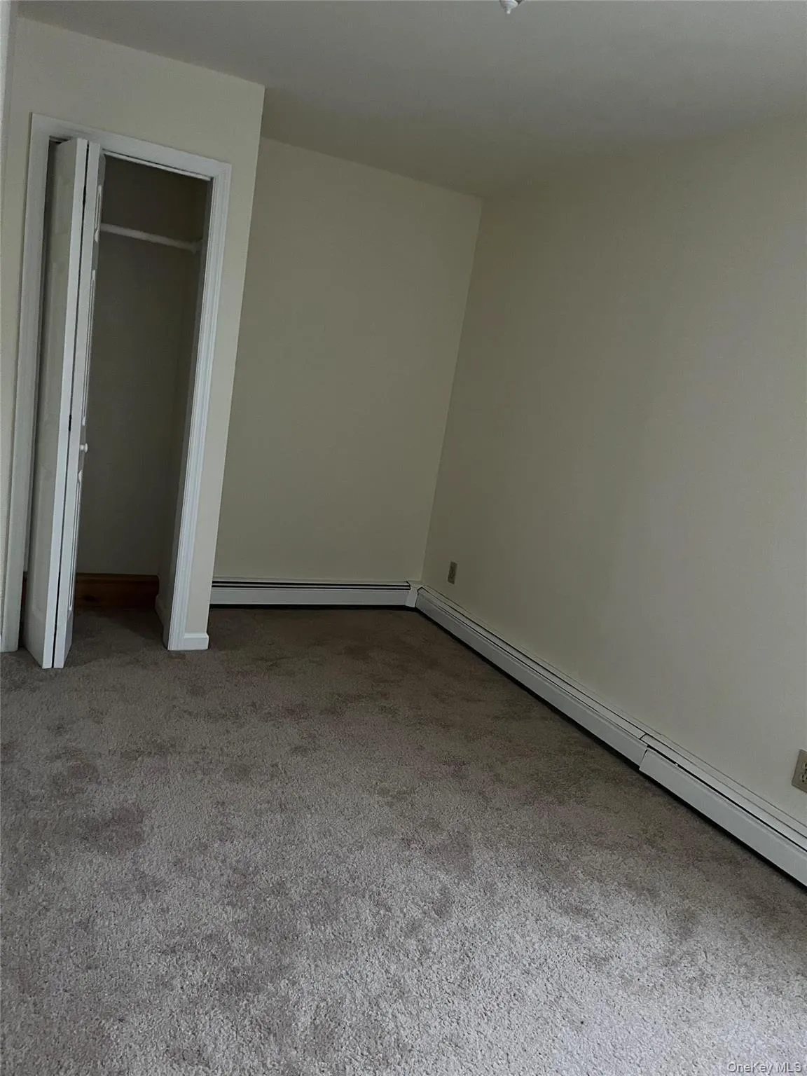 Unfurnished bedroom with baseboard heating, light colored carpet, and a closet Unfurnished bedroom with baseboard heating, light colored carpet, and a closet