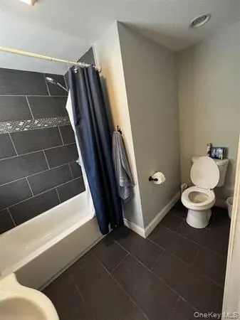 Full bath featuring shower / bathtub combination with curtain and dark tile patterned flooring Full bath featuring shower / bathtub combination with curtain and dark tile patterned flooring