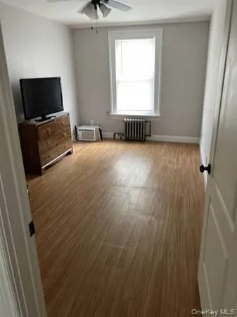 Unfurnished bedroom with wood finished floors, ceiling fan, and radiator Unfurnished bedroom with wood finished floors, ceiling fan, and radiator