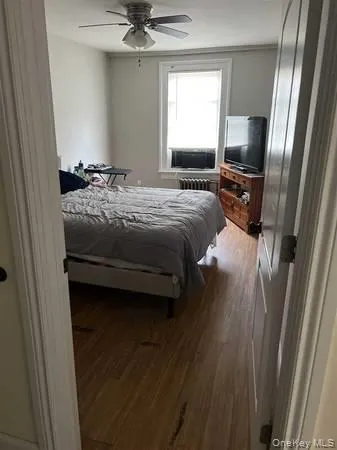 Bedroom featuring wood finished floors, a ceiling fan, and radiator heating unit Bedroom featuring wood finished floors, a ceiling fan, and radiator heating unit