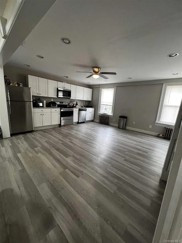 Kitchen with white cabinetry, stainless steel appliances, light wood-style floors, open floor plan, and radiator Kitchen with white cabinetry, stainless steel appliances, light wood-style floors, open floor plan, and radiator