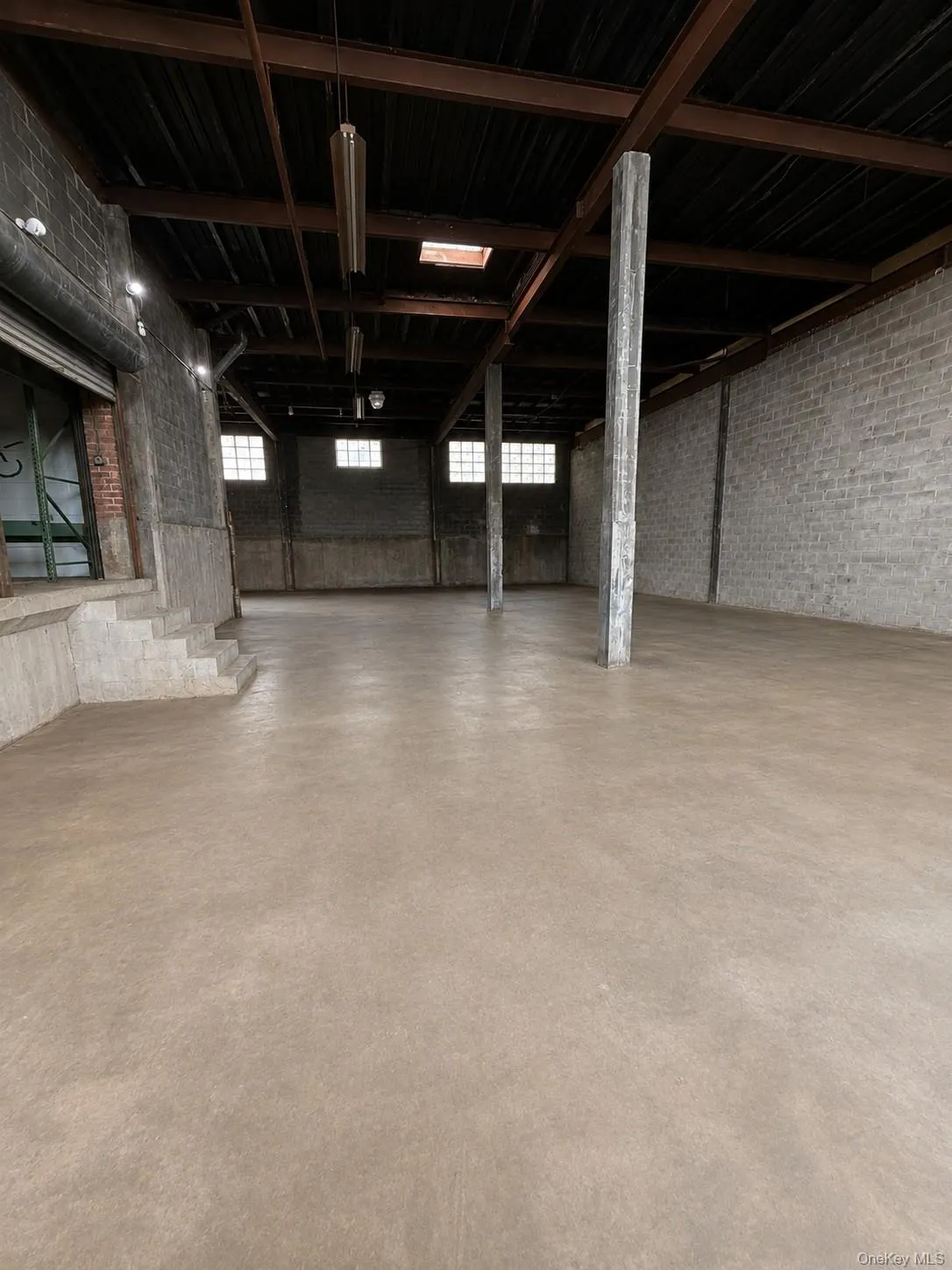 Expansive open-concept space featuring exposed structural beams, a concrete floor, and block walls Expansive open-concept space featuring exposed structural beams, a concrete floor, and block walls