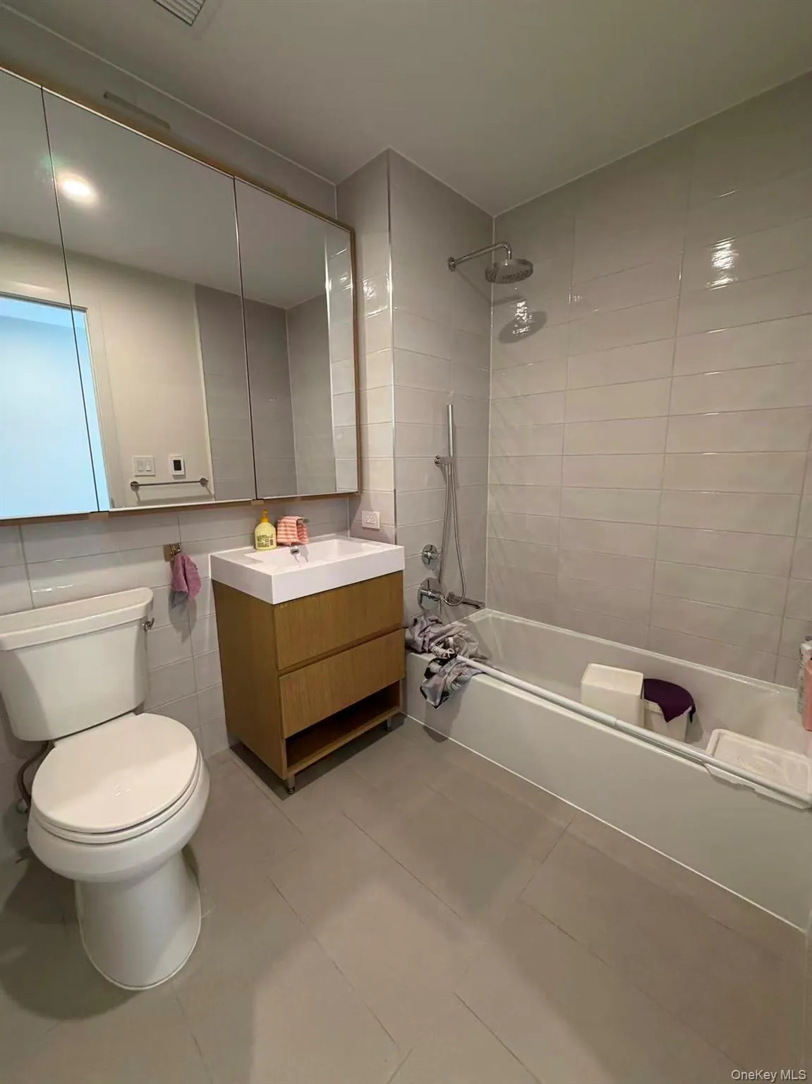 Bathroom with vanity, washtub / shower combination, light tile patterned floors, and tile walls Bathroom with vanity, washtub / shower combination, light tile patterned floors, and tile walls