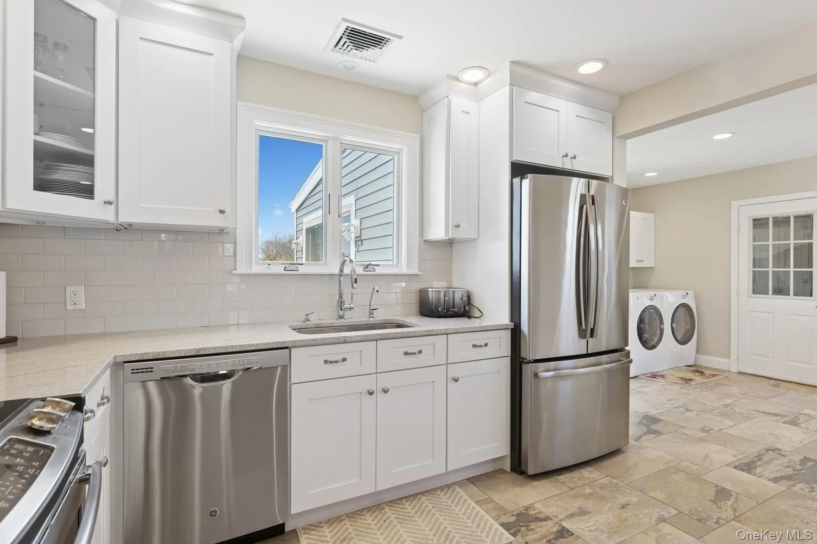Kitchen with washer and clothes dryer, appliances with stainless steel finishes, white cabinetry, light stone counters, and stone tile floors Kitchen with washer and clothes dryer, appliances with stainless steel finishes, white cabinetry, light stone counters, and stone tile floors