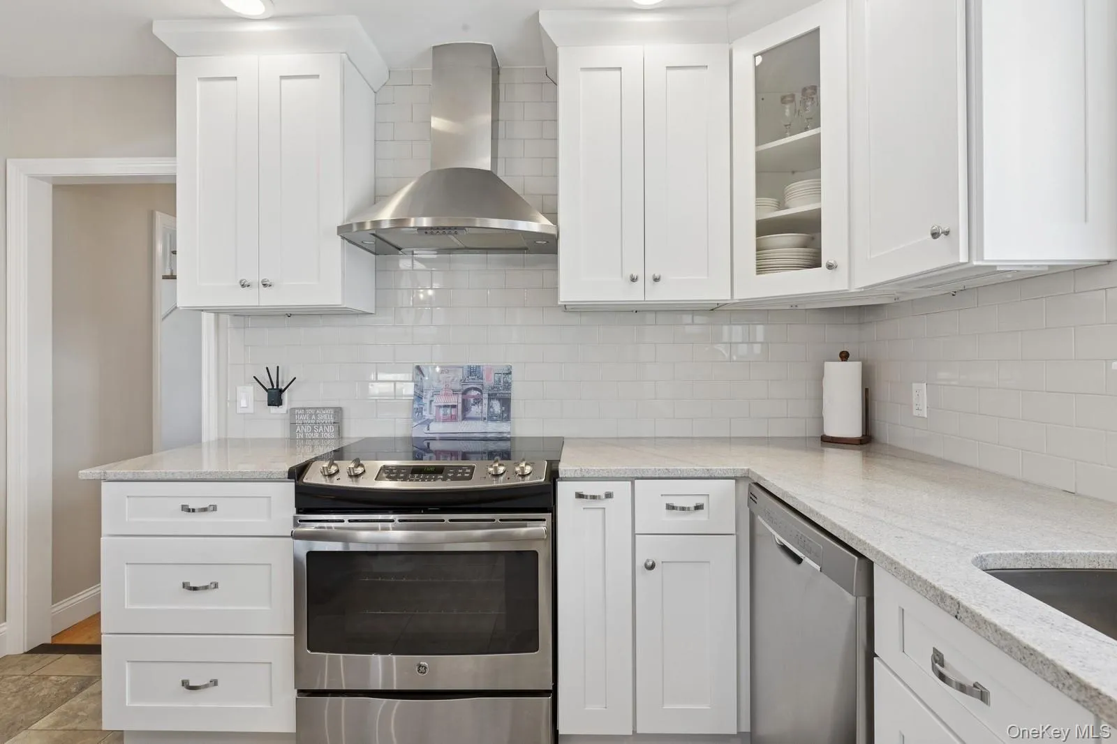 Kitchen with appliances with stainless steel finishes, wall chimney exhaust hood, light stone countertops, and white cabinetry Kitchen with appliances with stainless steel finishes, wall chimney exhaust hood, light stone countertops, and white cabinetry