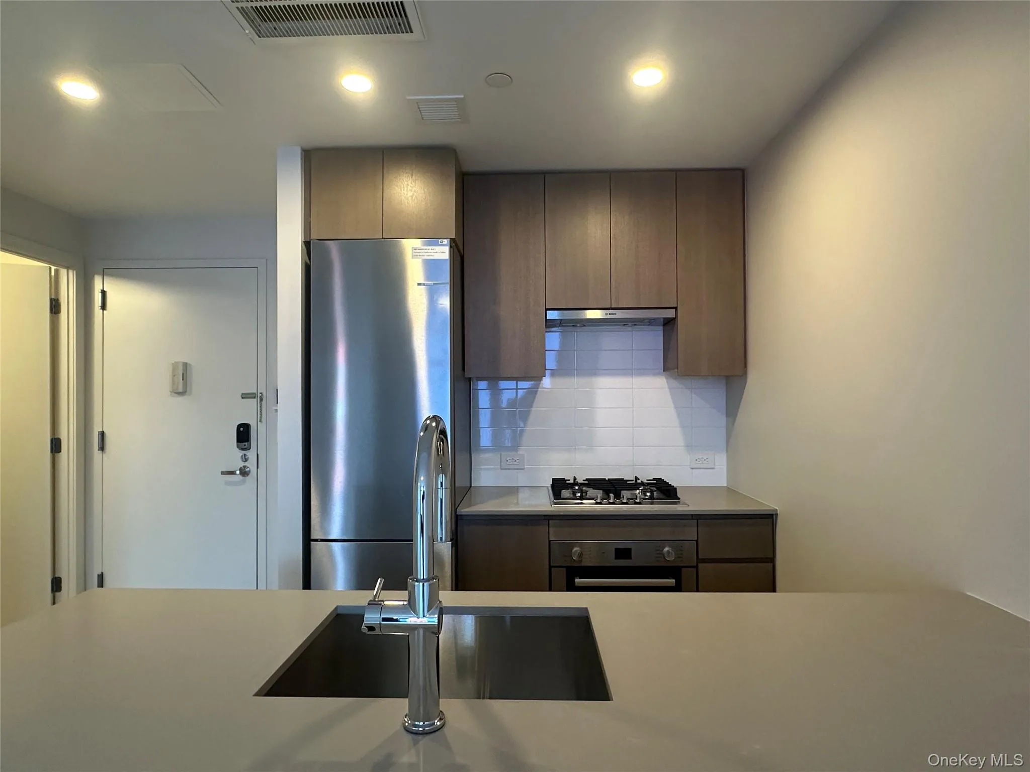 Kitchen featuring stainless steel appliances, visible vents, under cabinet range hood, light countertops, and tasteful backsplash Kitchen featuring stainless steel appliances, visible vents, under cabinet range hood, light countertops, and tasteful backsplash