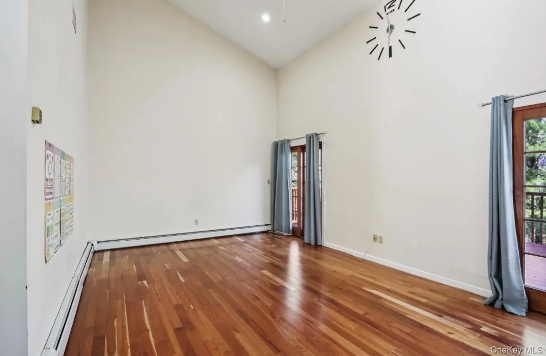 Empty room with high vaulted ceiling, baseboard heating, dark wood-style floors, and healthy amount of natural light Empty room with high vaulted ceiling, baseboard heating, dark wood-style floors, and healthy amount of natural light