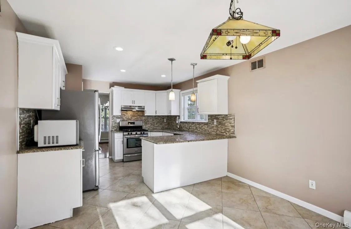 Kitchen with dark stone countertops, white cabinets, appliances with stainless steel finishes, a peninsula, and hanging light fixtures Kitchen with dark stone countertops, white cabinets, appliances with stainless steel finishes, a peninsula, and hanging light fixtures