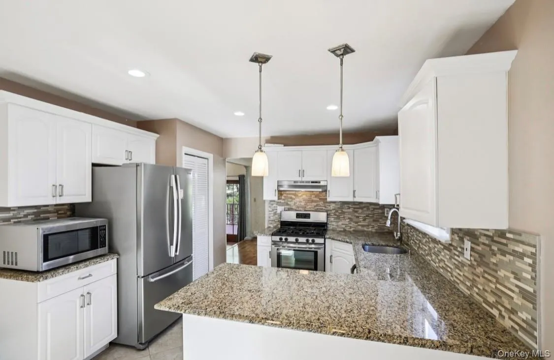 Kitchen featuring dark stone counters, backsplash, stainless steel appliances, decorative light fixtures, and recessed lighting Kitchen featuring dark stone counters, backsplash, stainless steel appliances, decorative light fixtures, and recessed lighting