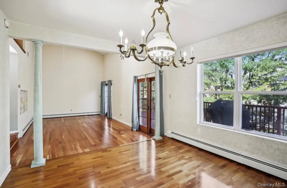 Unfurnished dining area featuring a baseboard heating unit, hardwood / wood-style floors, and decorative columns Unfurnished dining area featuring a baseboard heating unit, hardwood / wood-style floors, and decorative columns