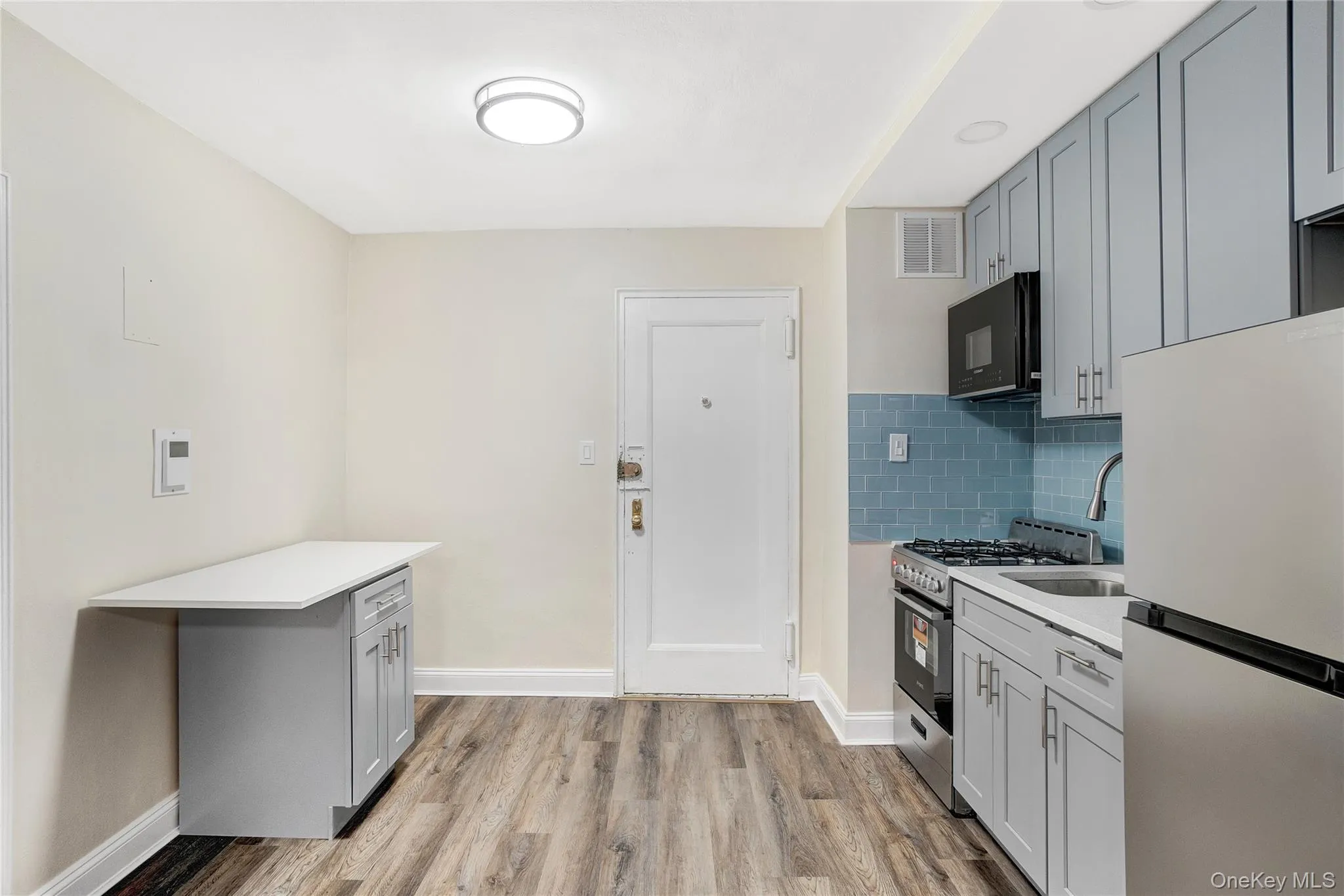 Kitchen with gray cabinets, freestanding refrigerator, stainless steel gas range oven, backsplash, and black microwave Kitchen with gray cabinets, freestanding refrigerator, stainless steel gas range oven, backsplash, and black microwave