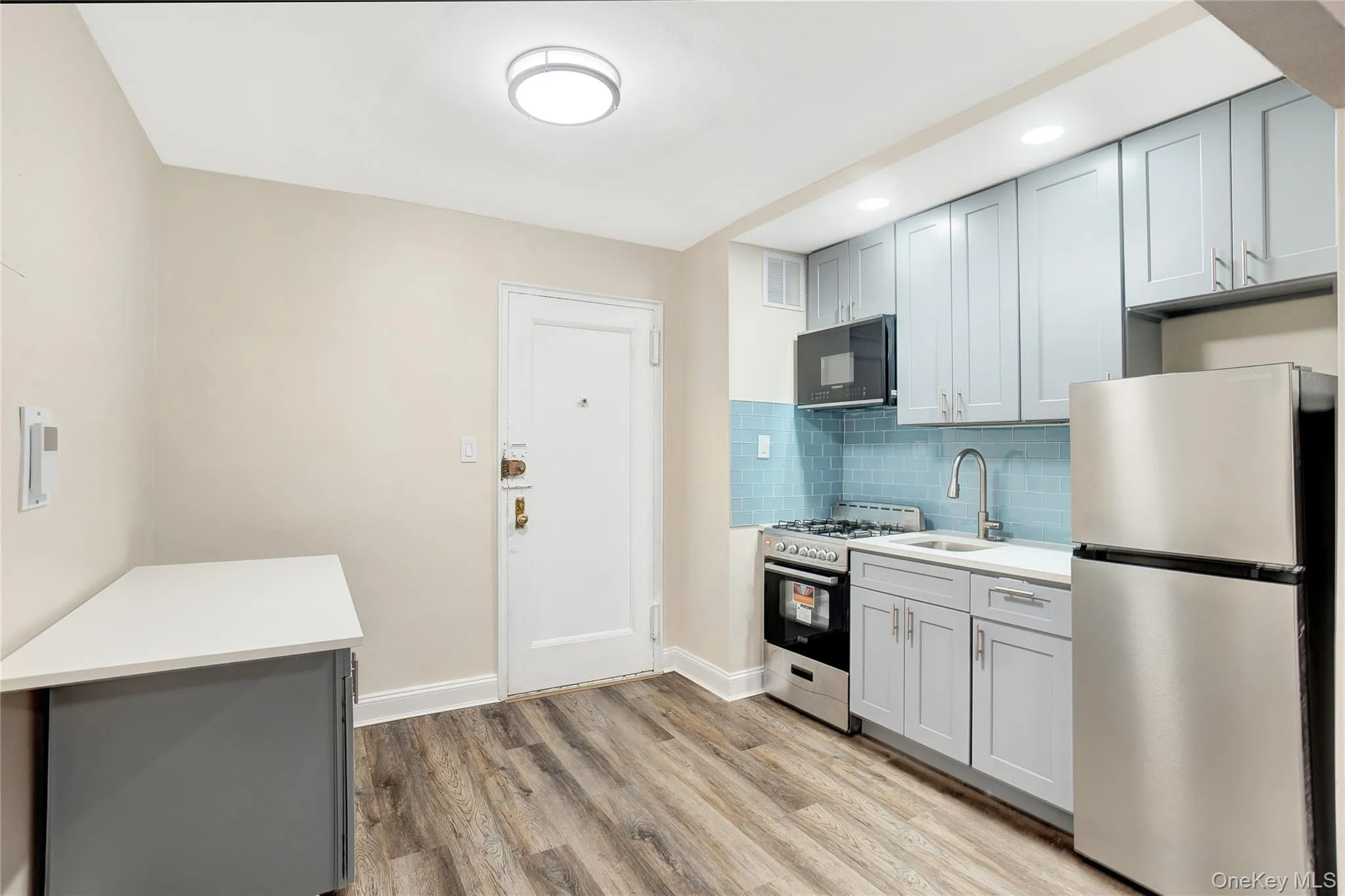 Kitchen with gray cabinets, appliances with stainless steel finishes, backsplash, and light wood-style floors Kitchen with gray cabinets, appliances with stainless steel finishes, backsplash, and light wood-style floors