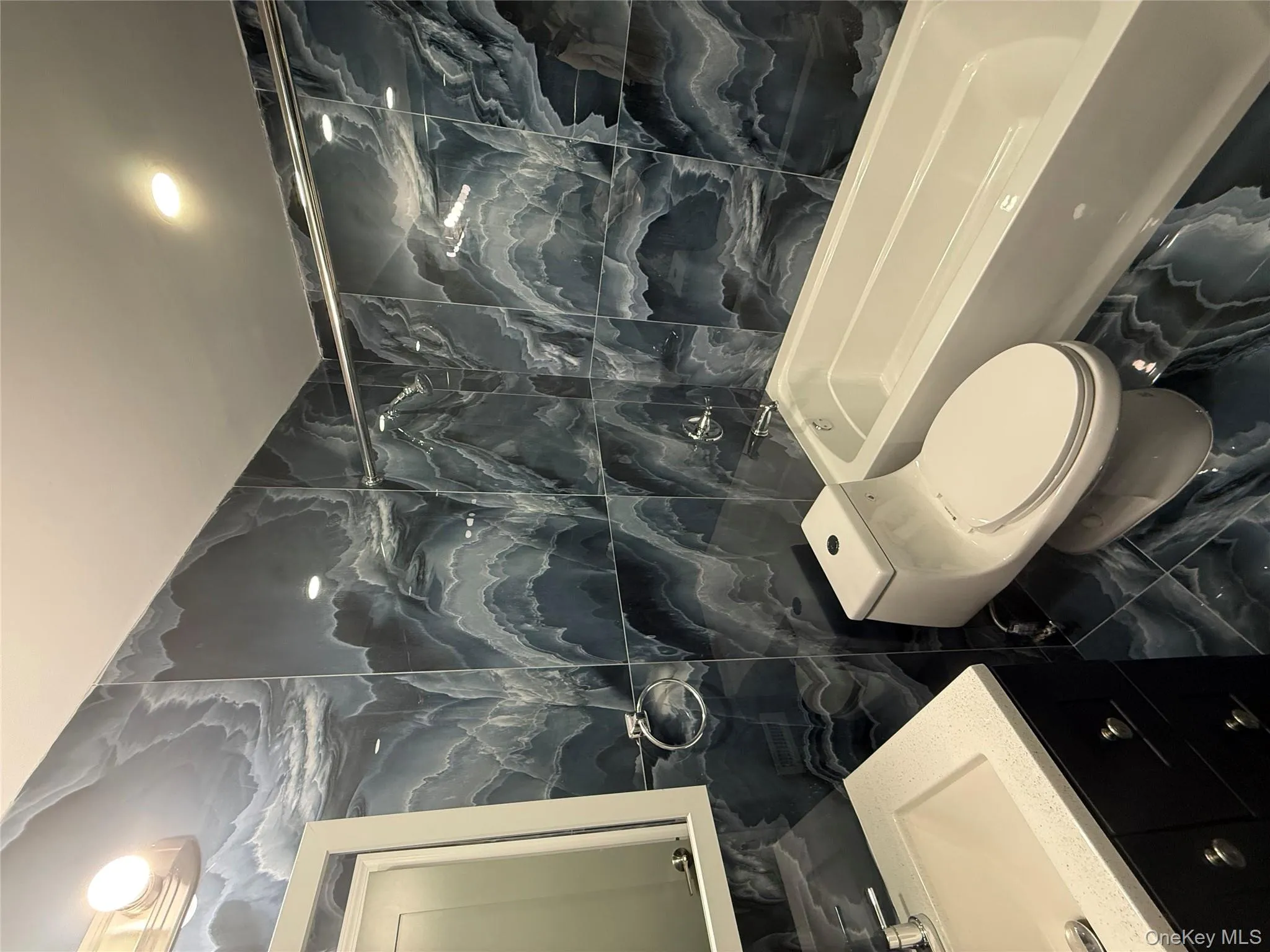 Full bathroom with tile walls, marble look tiles, vanity, shower / bathtub combination, and recessed lighting Full bathroom with tile walls, marble look tiles, vanity, shower / bathtub combination, and recessed lighting