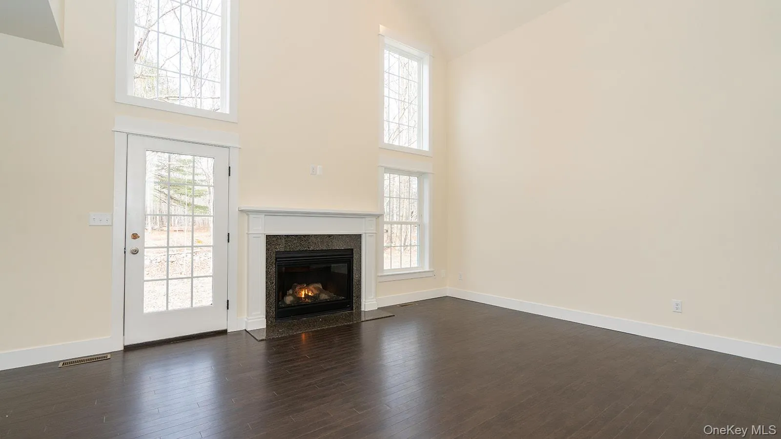 Unfurnished living room with high vaulted ceiling, dark wood finished floors, a fireplace, and healthy amount of natural light Unfurnished living room with high vaulted ceiling, dark wood finished floors, a fireplace, and healthy amount of natural light