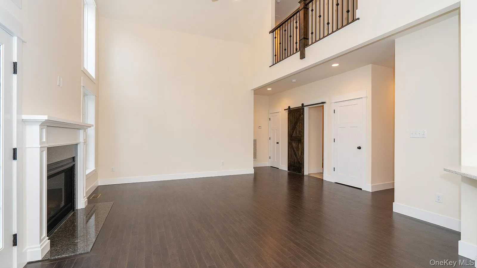 Unfurnished living room with a barn door, dark wood-style floors, a towering ceiling, a fireplace, and recessed lighting Unfurnished living room with a barn door, dark wood-style floors, a towering ceiling, a fireplace, and recessed lighting