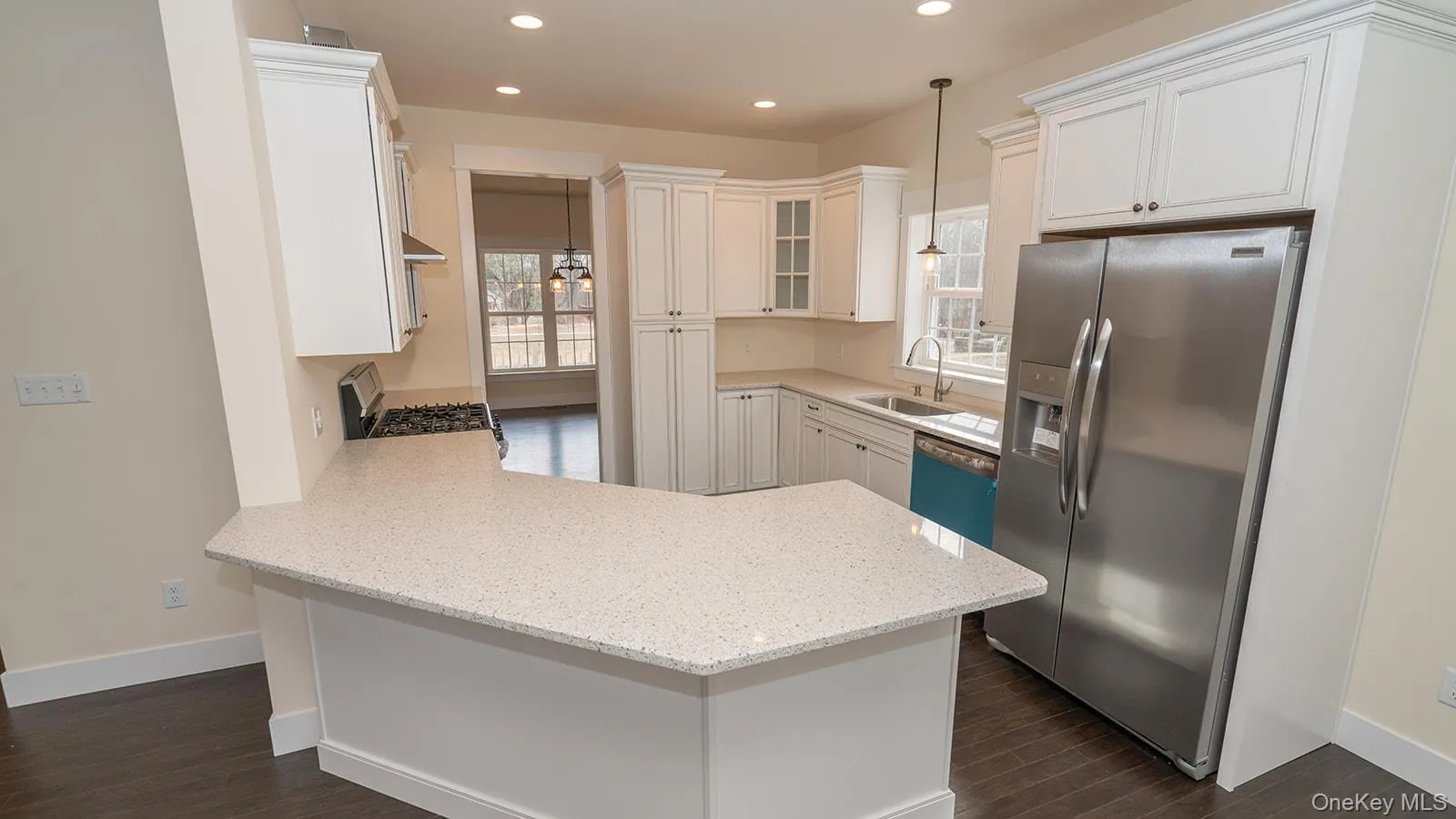 Kitchen featuring glass insert cabinets, appliances with stainless steel finishes, a peninsula, light stone counters, and hanging light fixtures Kitchen featuring glass insert cabinets, appliances with stainless steel finishes, a peninsula, light stone counters, and hanging light fixtures