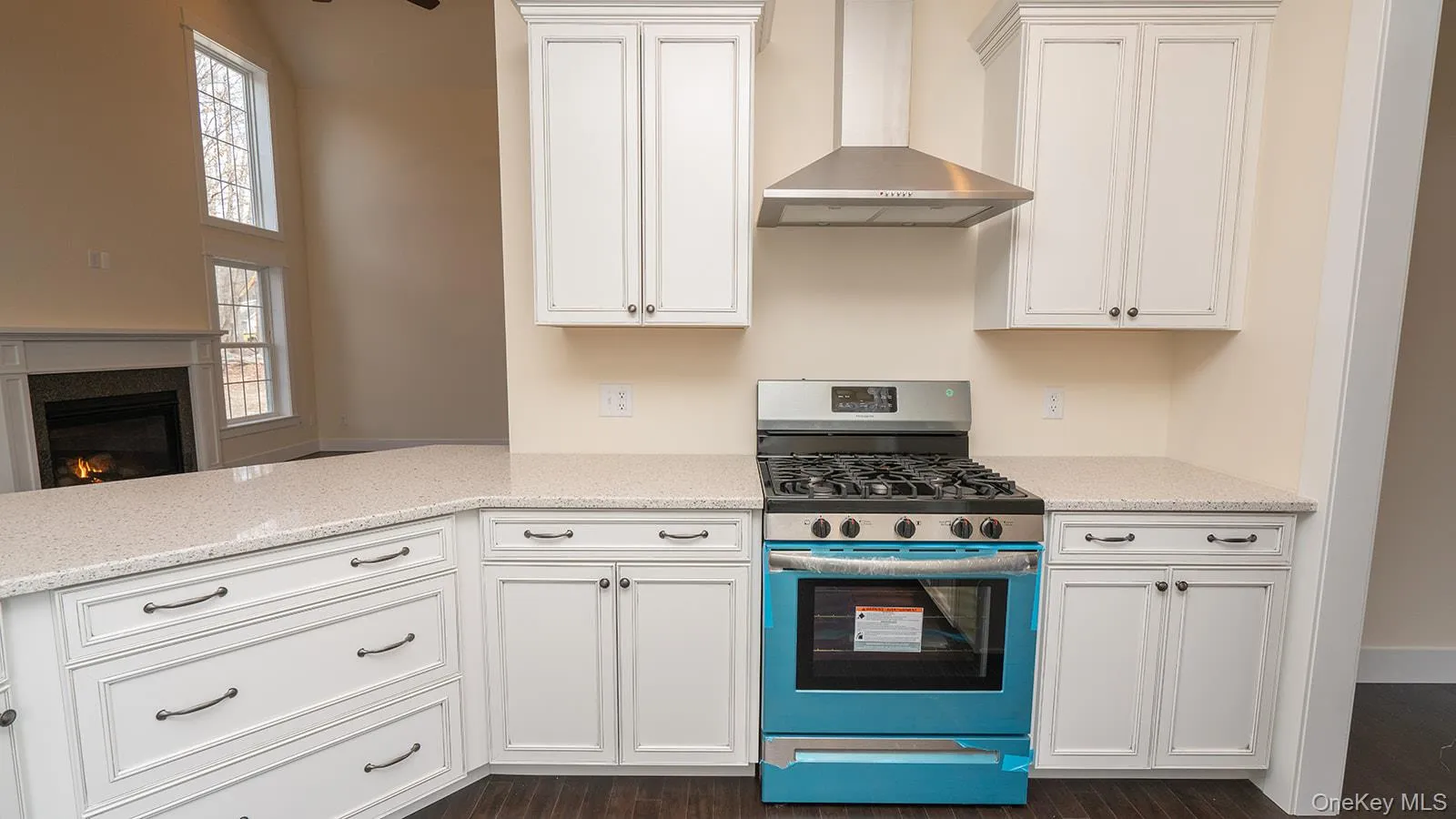 Kitchen featuring stainless steel gas stove, wall chimney exhaust hood, white cabinetry, a glass covered fireplace, and light stone countertops Kitchen featuring stainless steel gas stove, wall chimney exhaust hood, white cabinetry, a glass covered fireplace, and light stone countertops