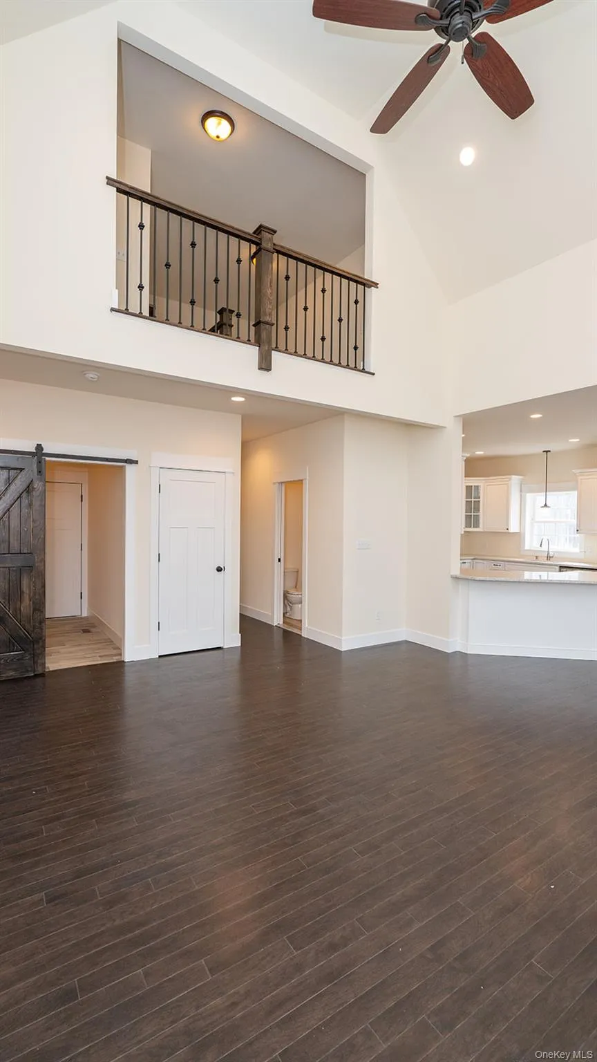 Unfurnished living room with a barn door, high vaulted ceiling, dark wood finished floors, recessed lighting, and a ceiling fan Unfurnished living room with a barn door, high vaulted ceiling, dark wood finished floors, recessed lighting, and a ceiling fan