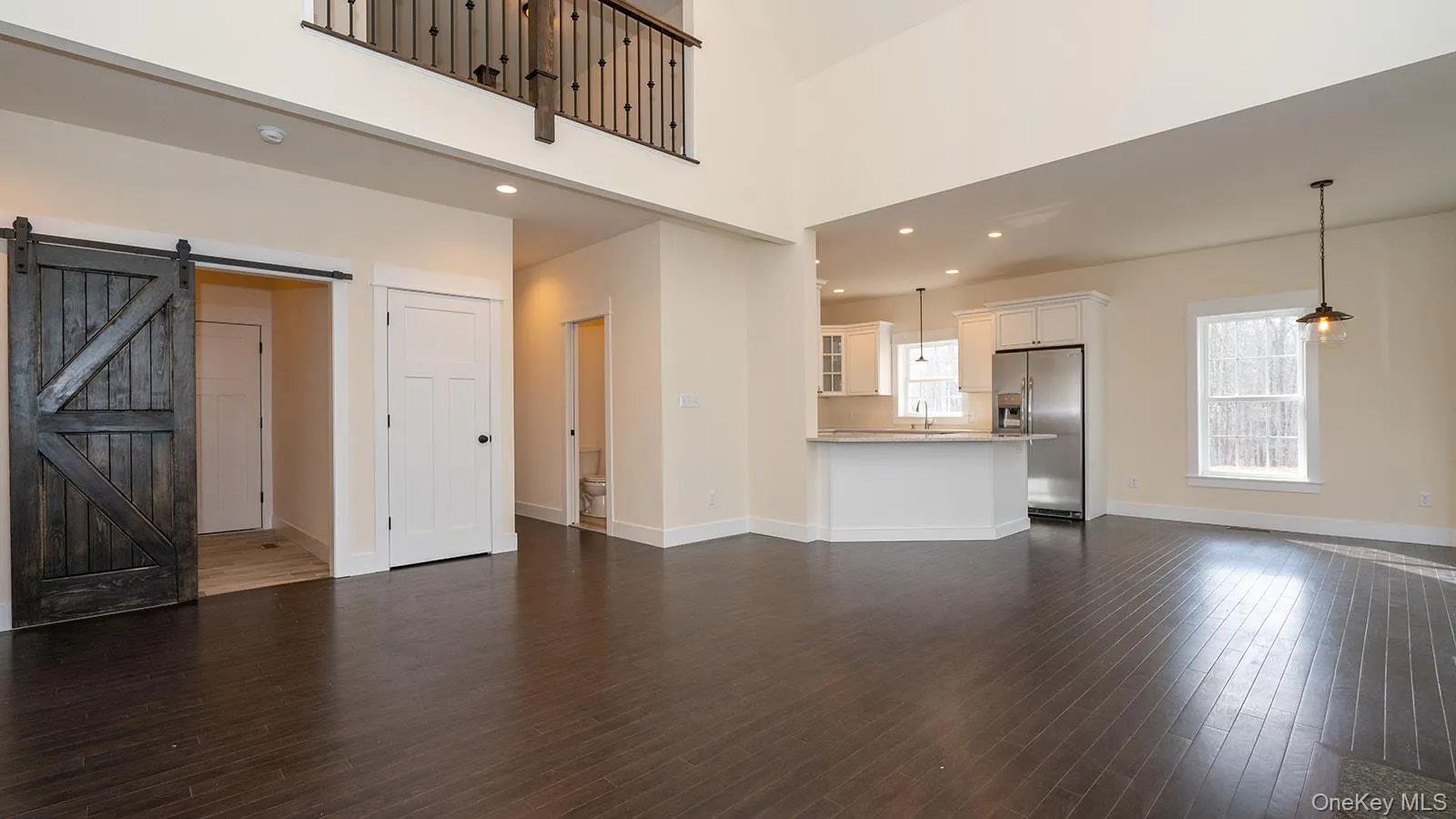 Unfurnished living room with a barn door, recessed lighting, a high ceiling, and dark wood-style flooring Unfurnished living room with a barn door, recessed lighting, a high ceiling, and dark wood-style flooring