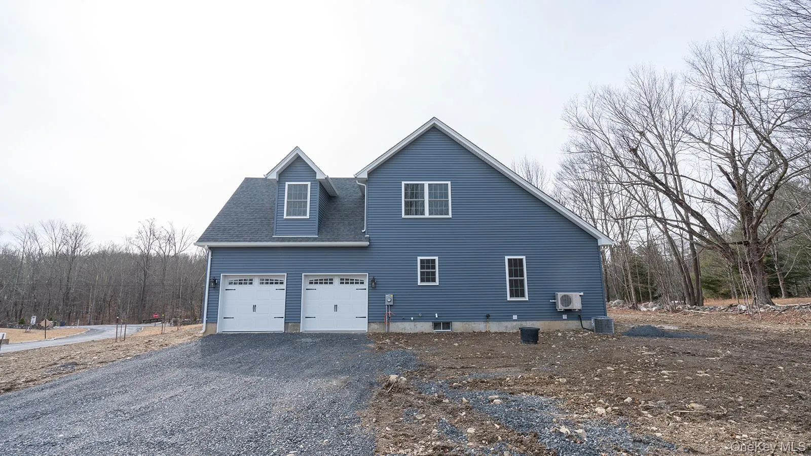 View of side of home featuring driveway, a shingled roof, and a view of trees View of side of home featuring driveway, a shingled roof, and a view of trees