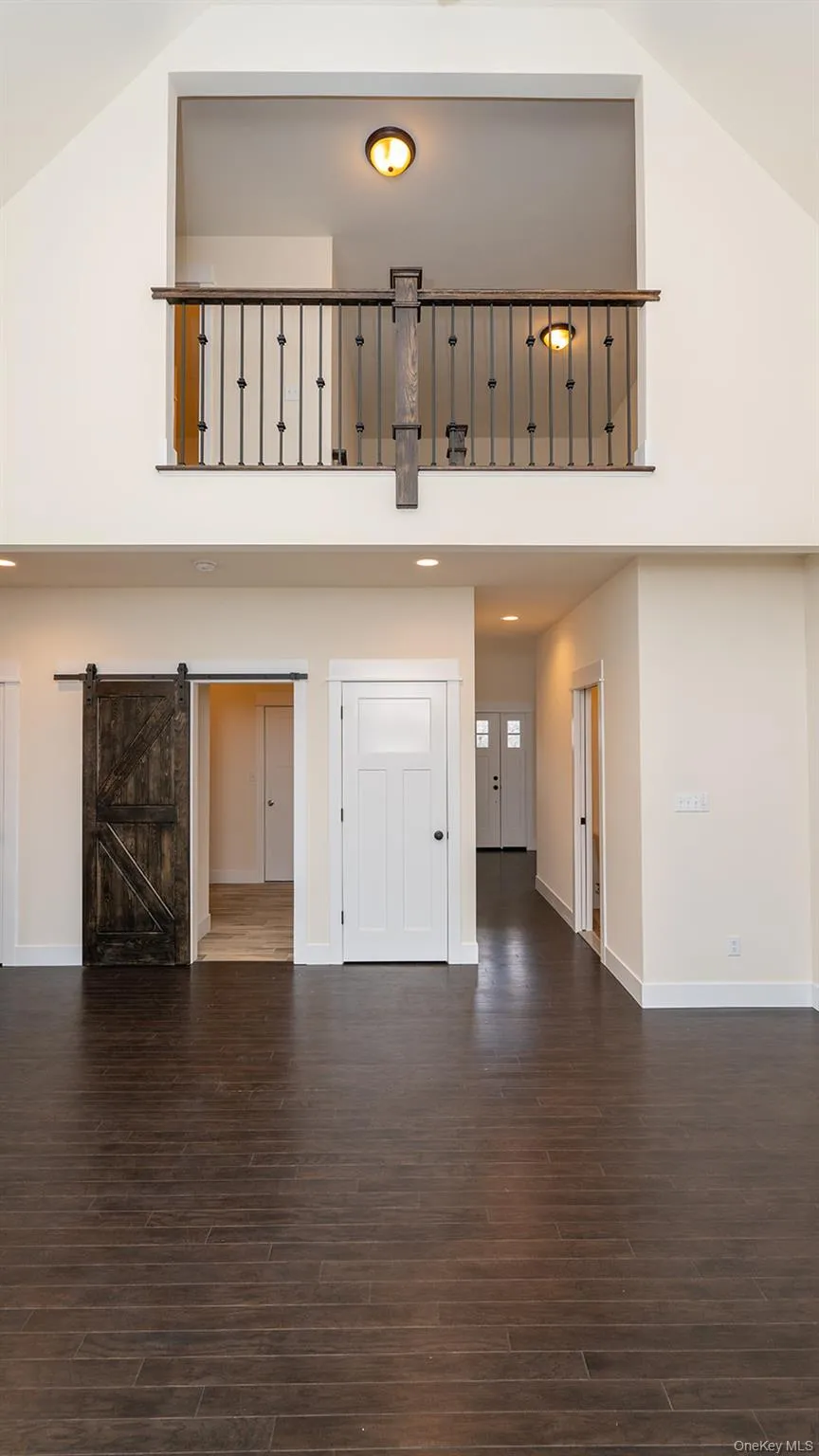 Unfurnished living room featuring high vaulted ceiling, a barn door, and dark wood-style flooring Unfurnished living room featuring high vaulted ceiling, a barn door, and dark wood-style flooring