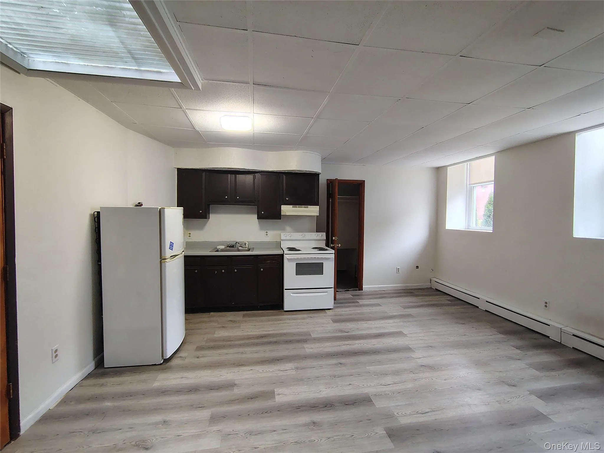 Kitchen with white appliances, light countertops, light wood-type flooring, a drop ceiling, and under cabinet range hood Kitchen with white appliances, light countertops, light wood-type flooring, a drop ceiling, and under cabinet range hood