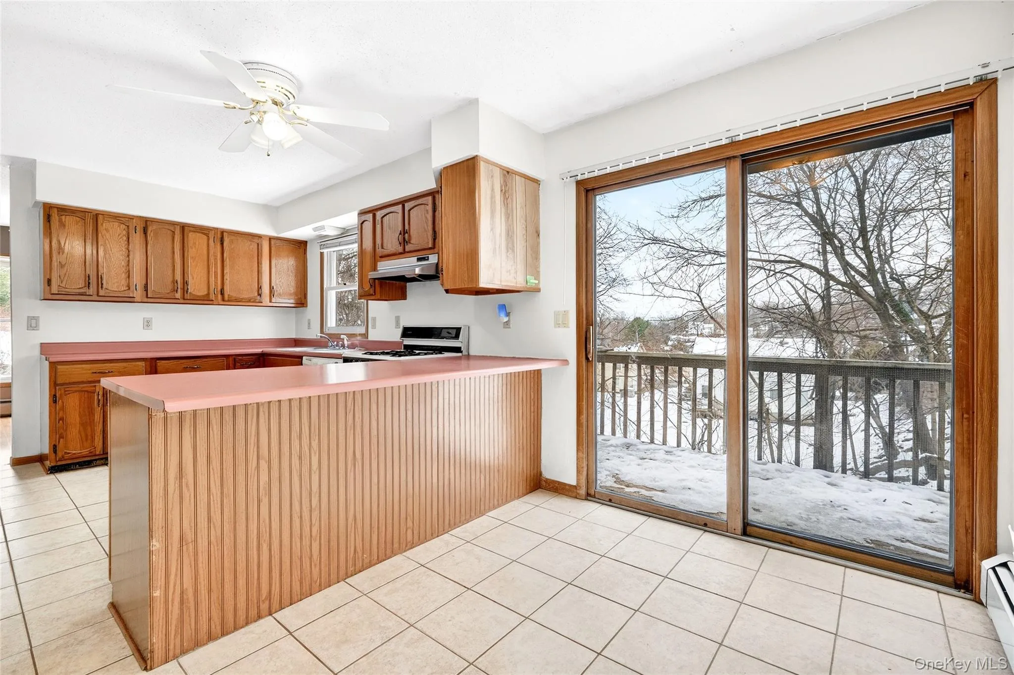 Kitchen with brown cabinets, a peninsula, light countertops, ceiling fan, and light tile patterned flooring Kitchen with brown cabinets, a peninsula, light countertops, ceiling fan, and light tile patterned flooring