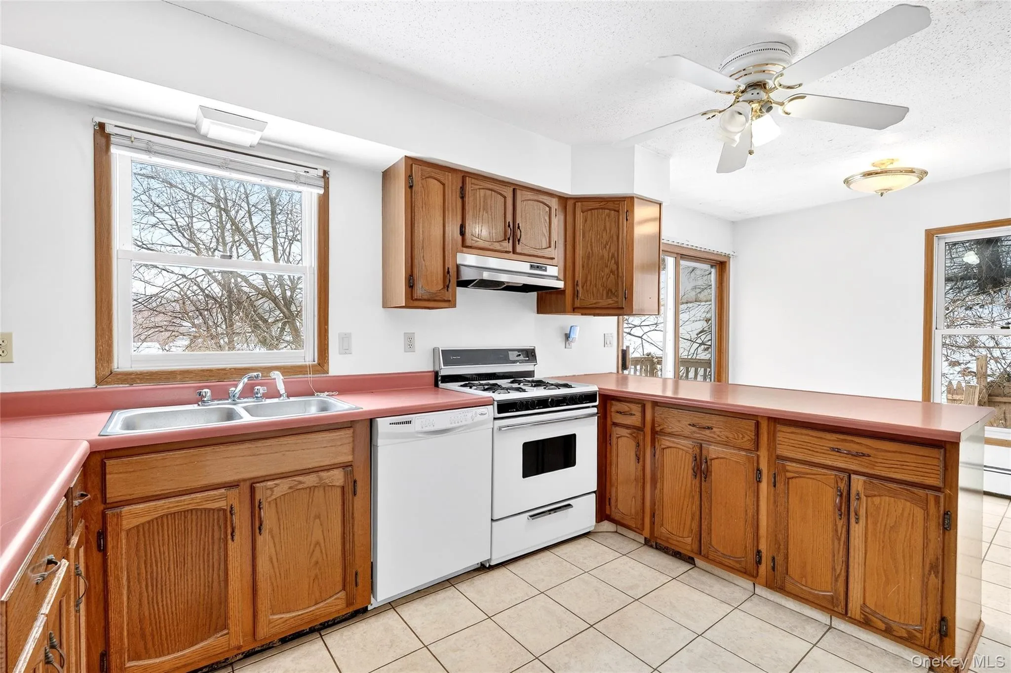 Kitchen featuring a peninsula, white appliances, brown cabinets, ceiling fan, and under cabinet range hood Kitchen featuring a peninsula, white appliances, brown cabinets, ceiling fan, and under cabinet range hood