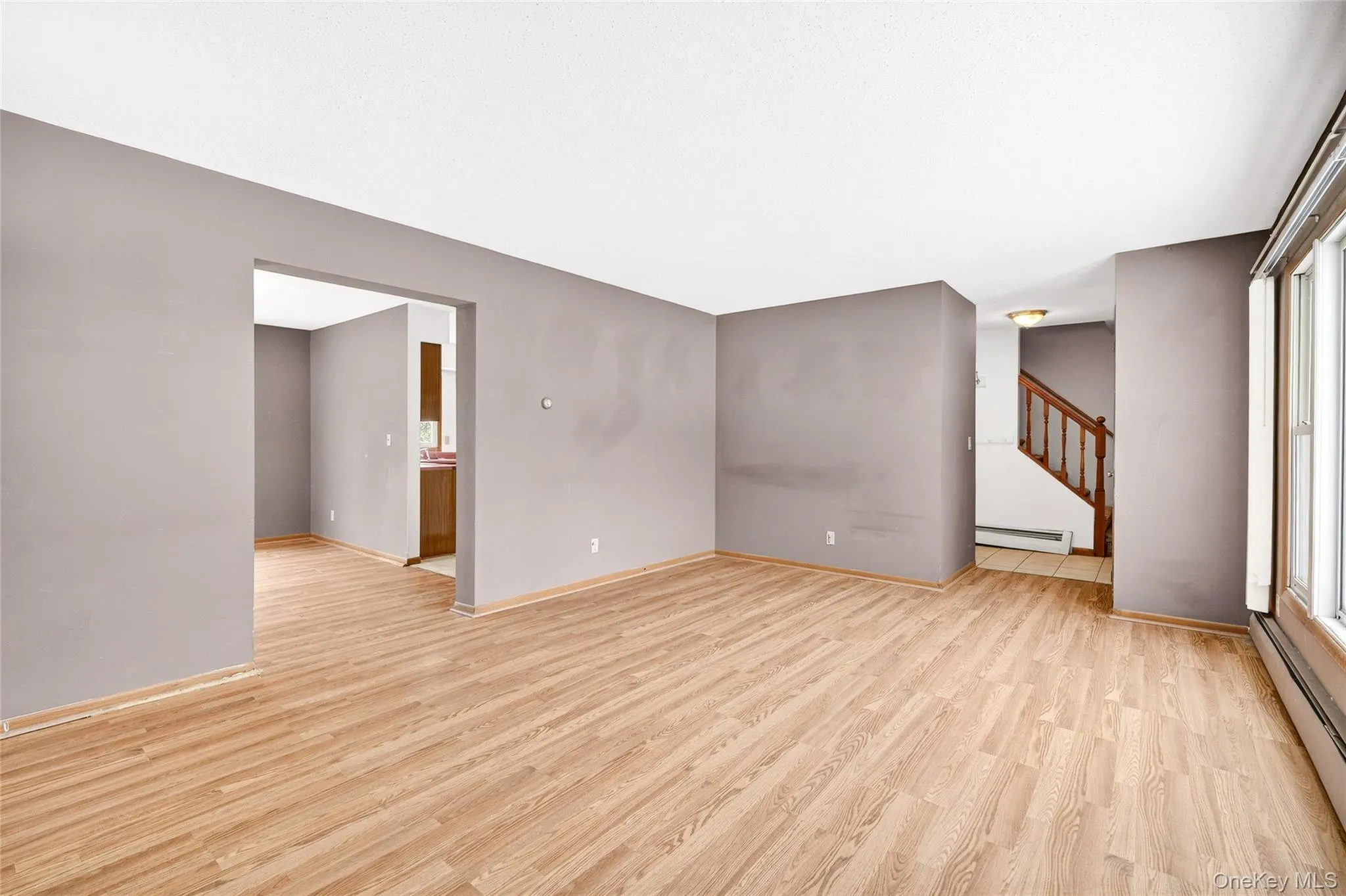 Spare room featuring baseboard heating, light wood-style floors, and stairs Spare room featuring baseboard heating, light wood-style floors, and stairs